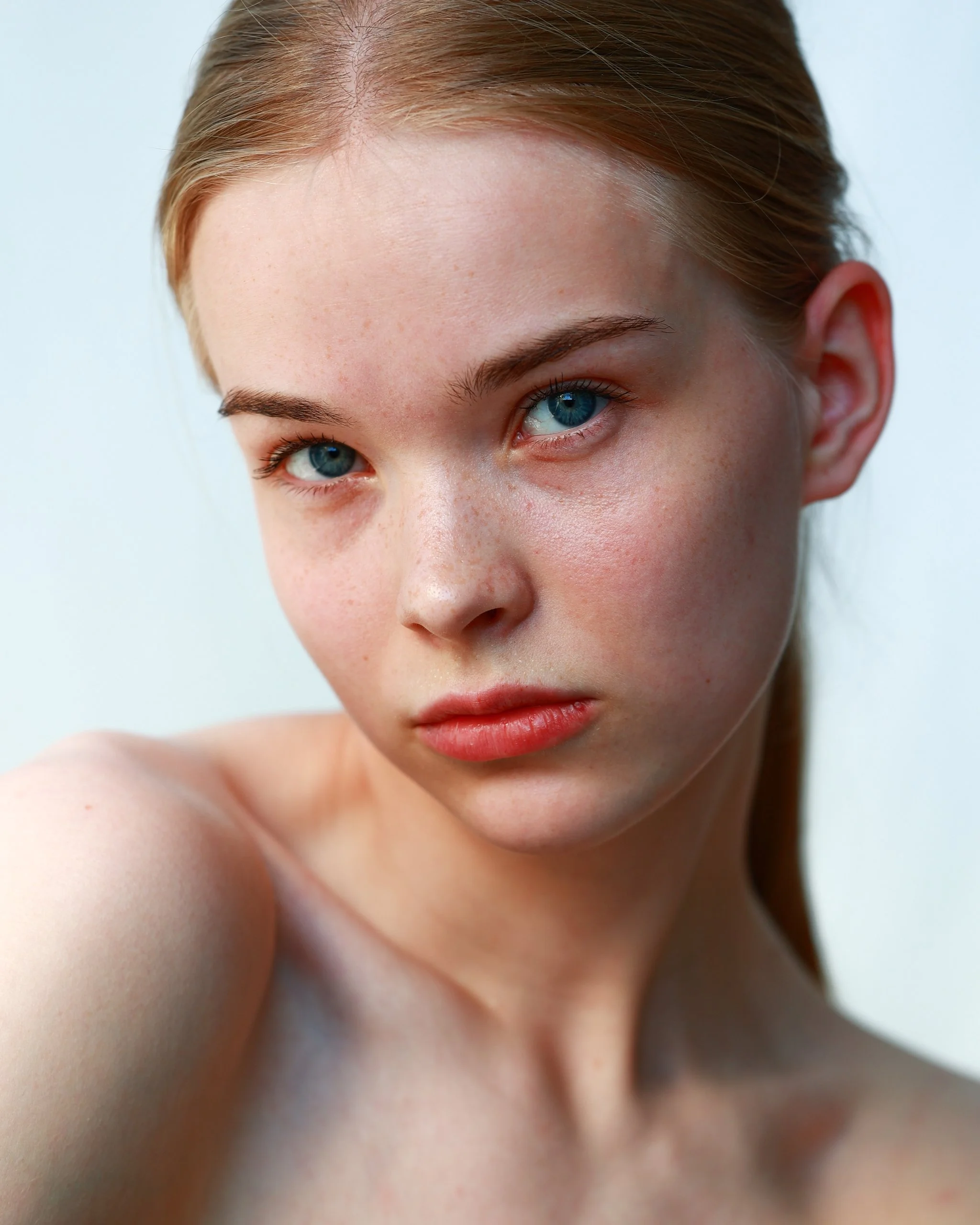 Close-up of a young woman with red hair, blue eyes, and light skin, looking directly at the camera.