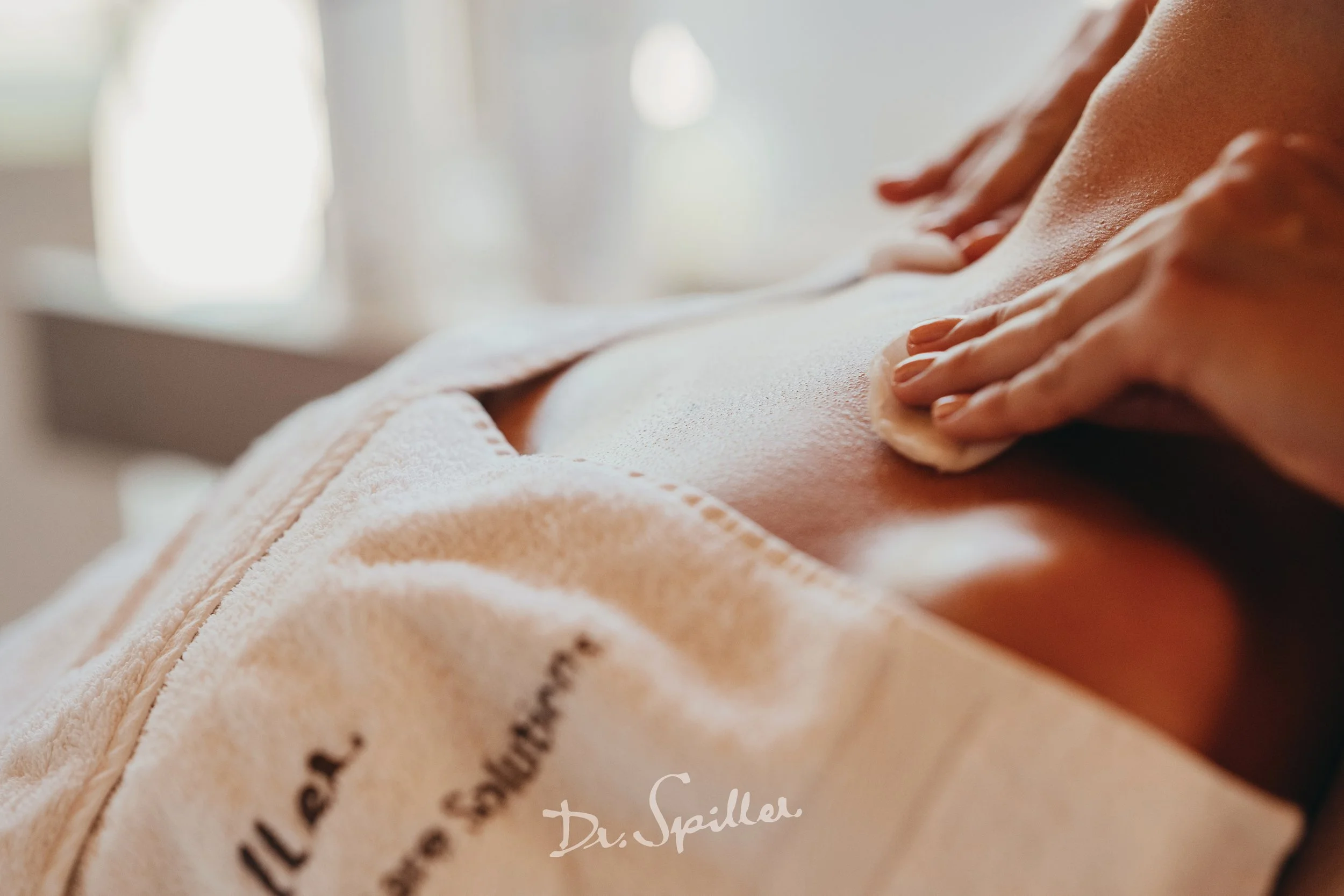 Dr Spiller Facial. A person getting a massage, with a focus on their back and shoulder area, using a white cloth or towel beneath them. Soft, natural light illuminating the scene.