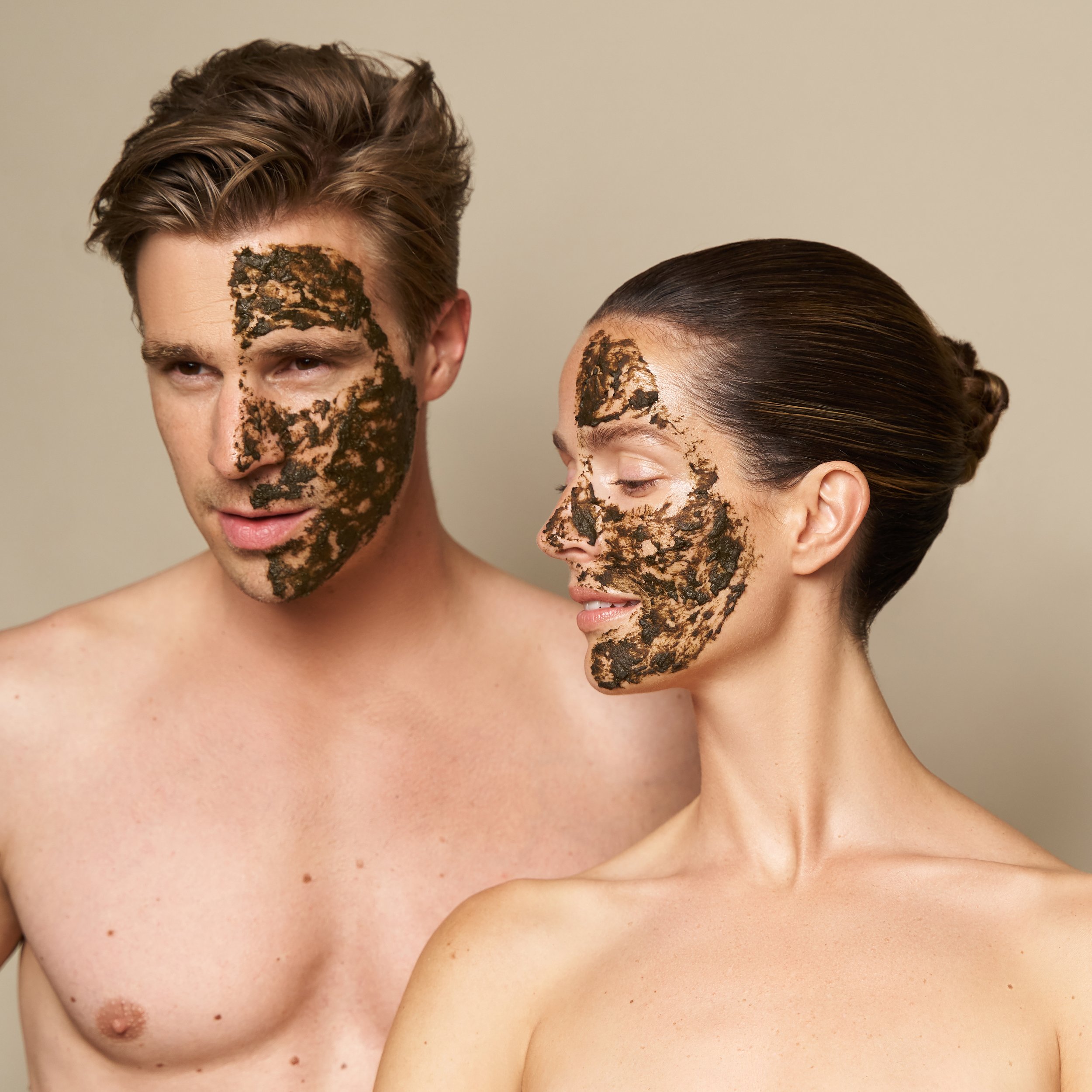 A man and a woman with dark green herbal mask by Herbs2Peel, a man and a woman topless and facing each other, with plain beige background. Sinead Quinn Facial Therapy