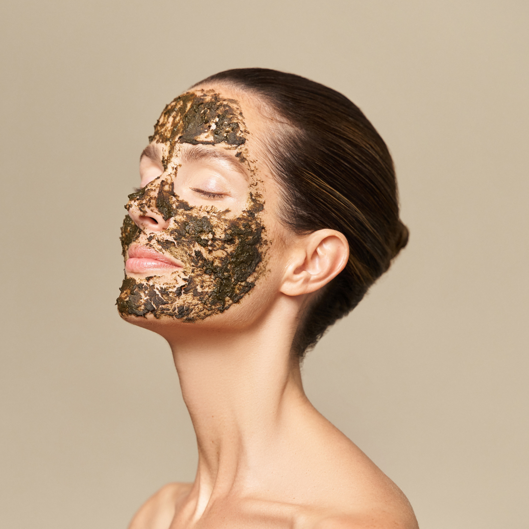 A woman with green herbal mask by Herbs2Peel facial mask applied on her face, with her eyes closed and head slightly tilted back, showing smooth skin and a neutral expression.