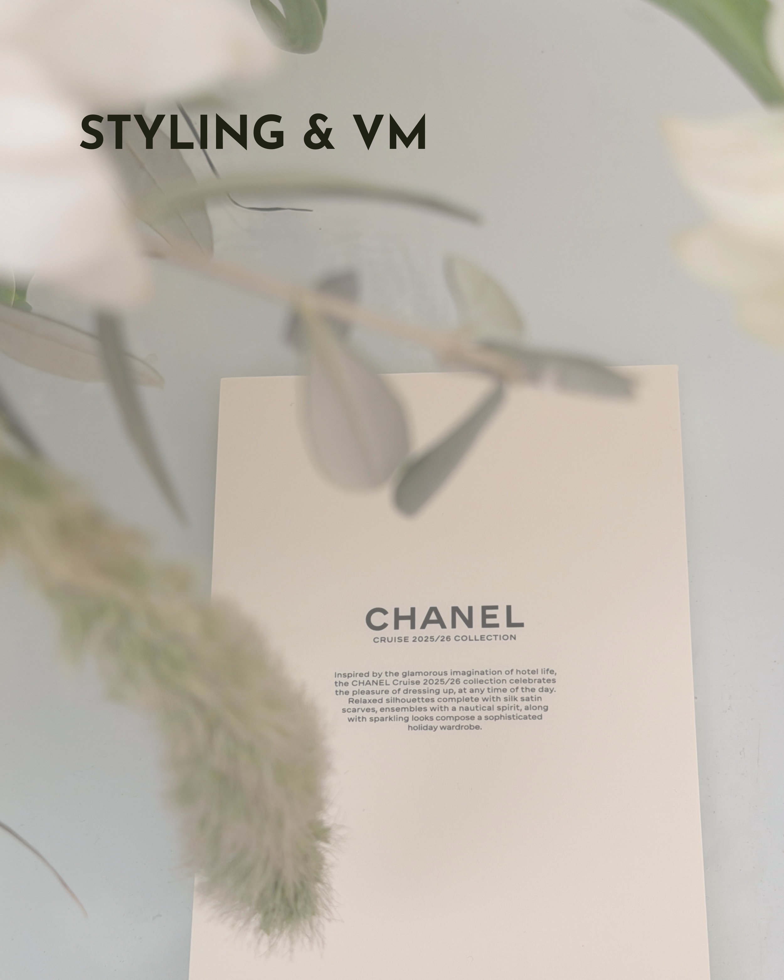 A Chanel booklet lays on a table with green foliage in the foreground