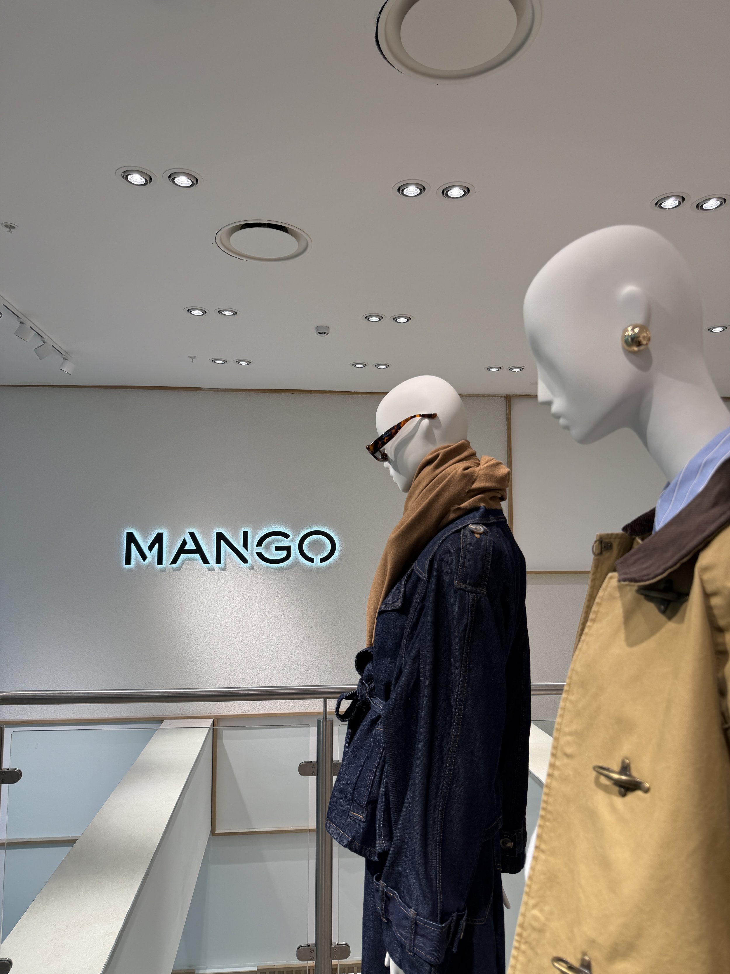 2 mannequins stood side profile in front of a Mango store sign.