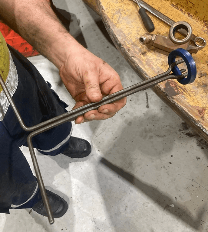 Person holding a metal tool with a blue circular handle, working at a cluttered workbench with various tools.
