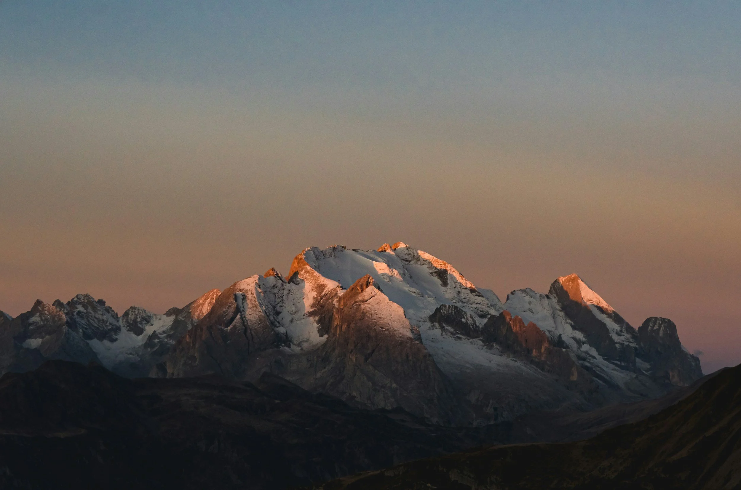 Snow-capped mountain range at sunset with a clear sky.
