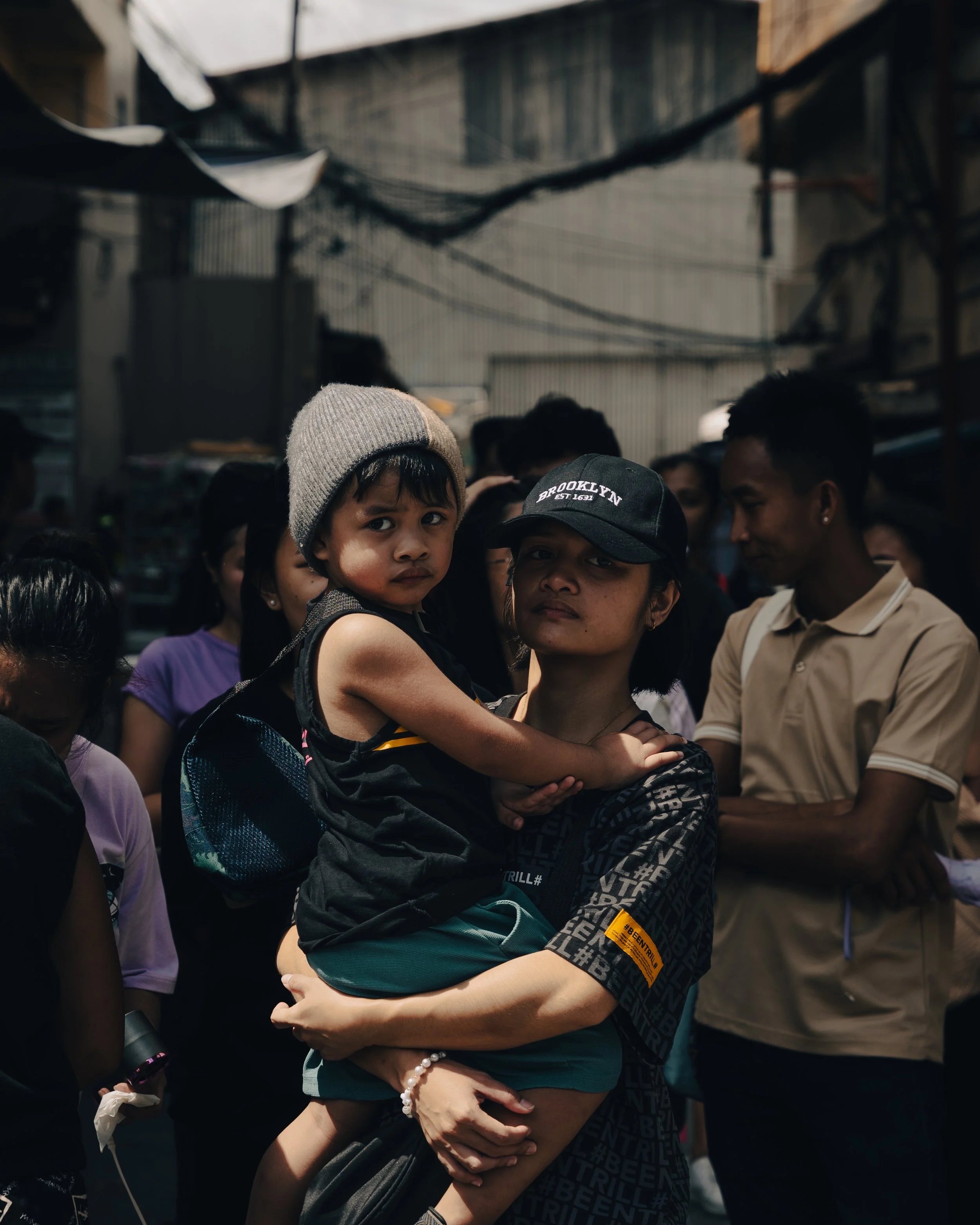A woman holding a young boy, surrounded by a crowd in an indoor market or gathering.