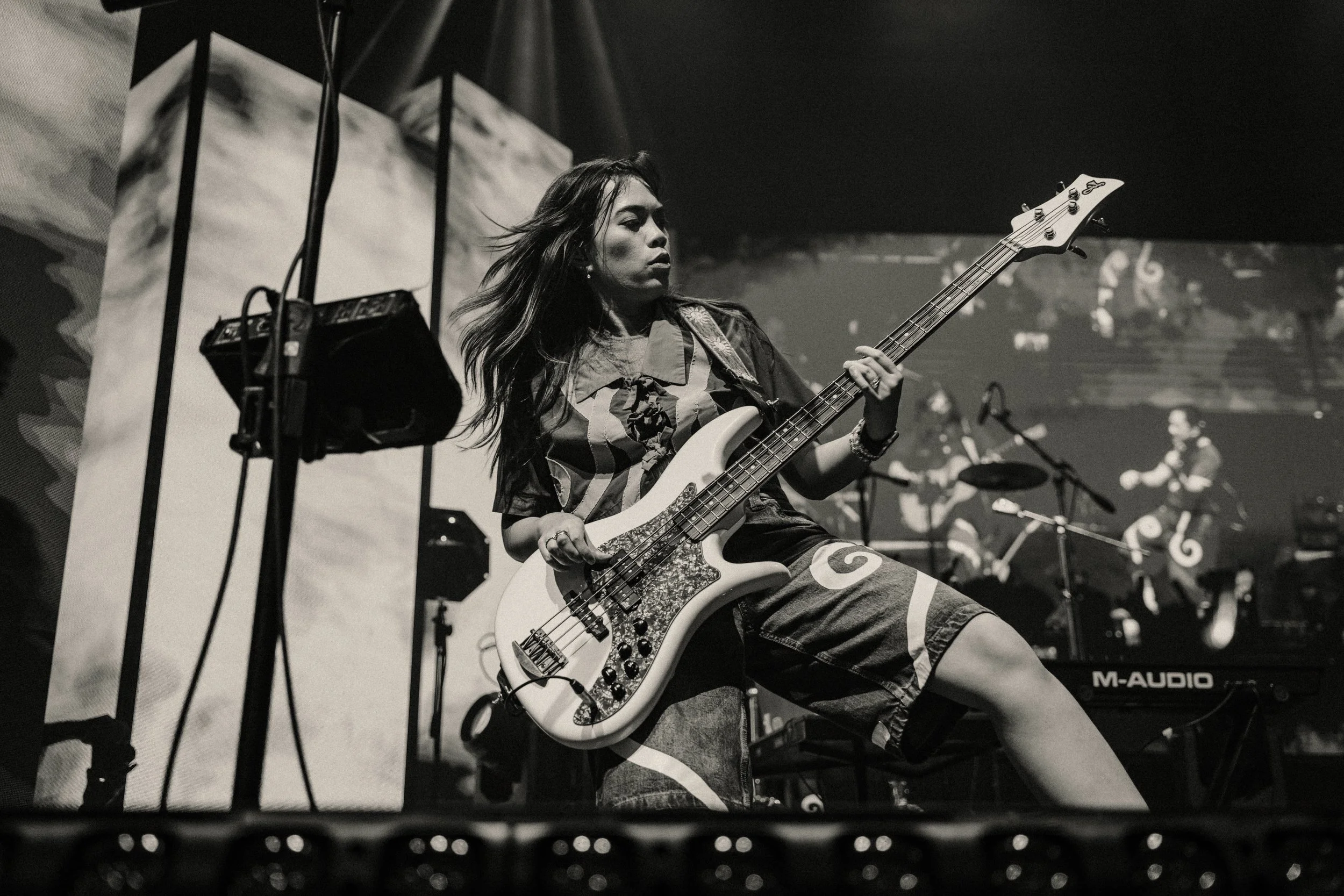 A woman playing an electric bass guitar on stage during a concert.