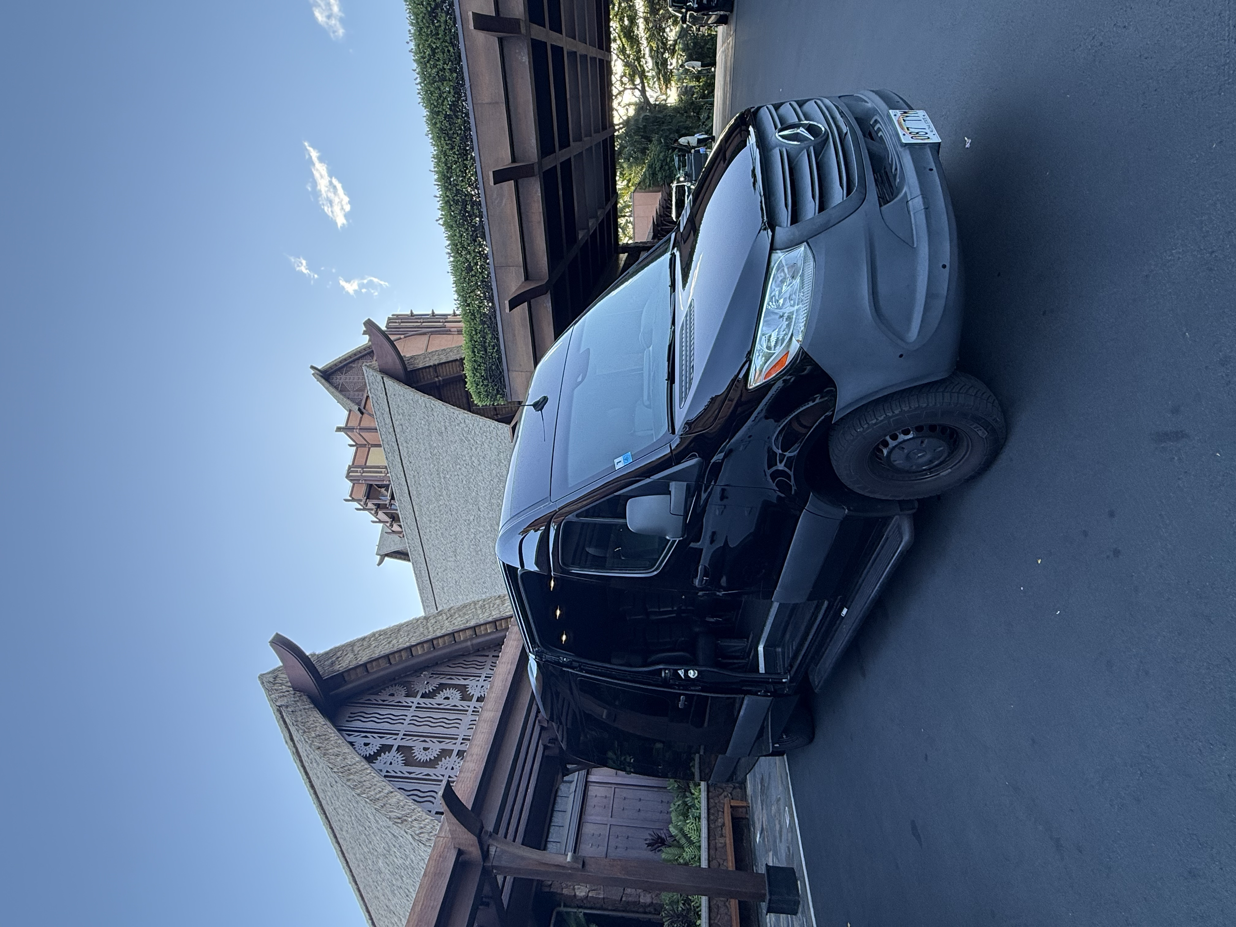 A white SUV parked in a driveway near a house with a roof overhang and garden bed; the sky is clear with a few clouds.