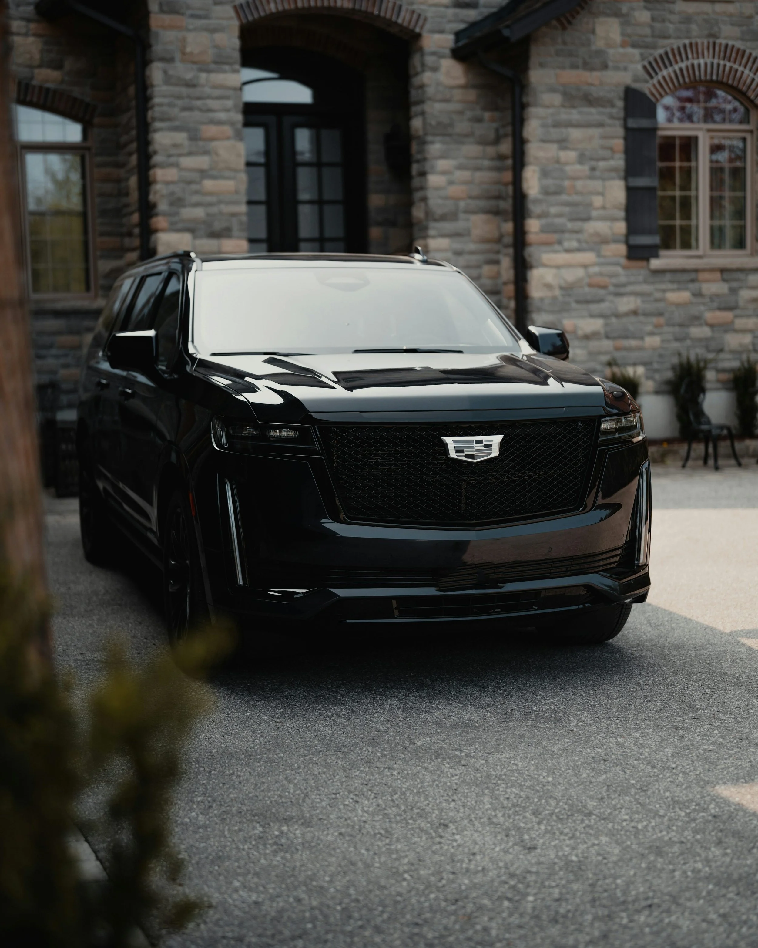 A black electric Cadillac SUV parked in front of a stone house.
