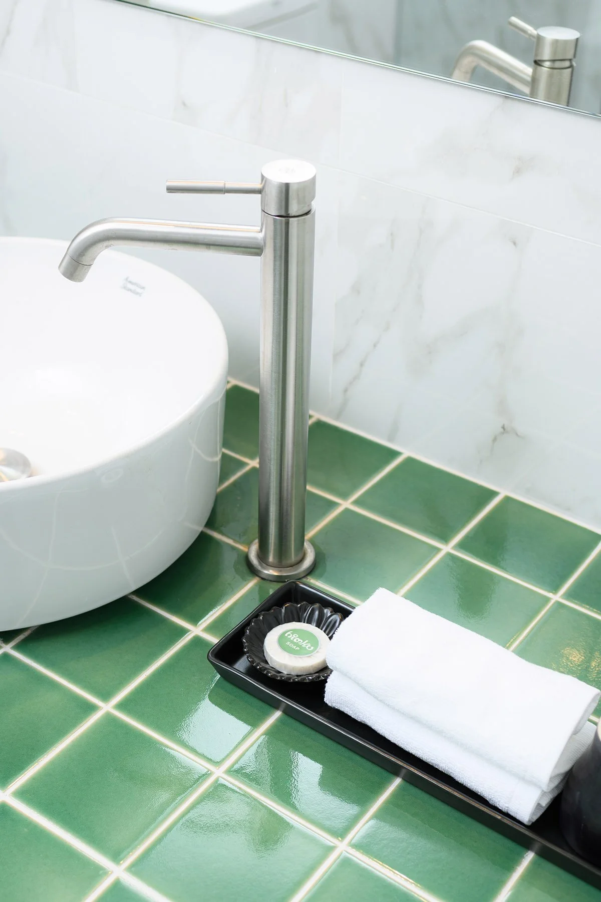 Bathroom sink with a modern silver faucet, a soap dish with soap, and a folded white towel on a green tiled countertop.