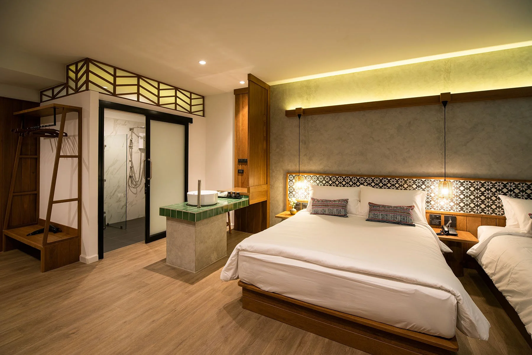 Hotel room with a large bed, nightstands, pendant lights, a bathroom with a walk-in shower, and a small green-tiled sink area.