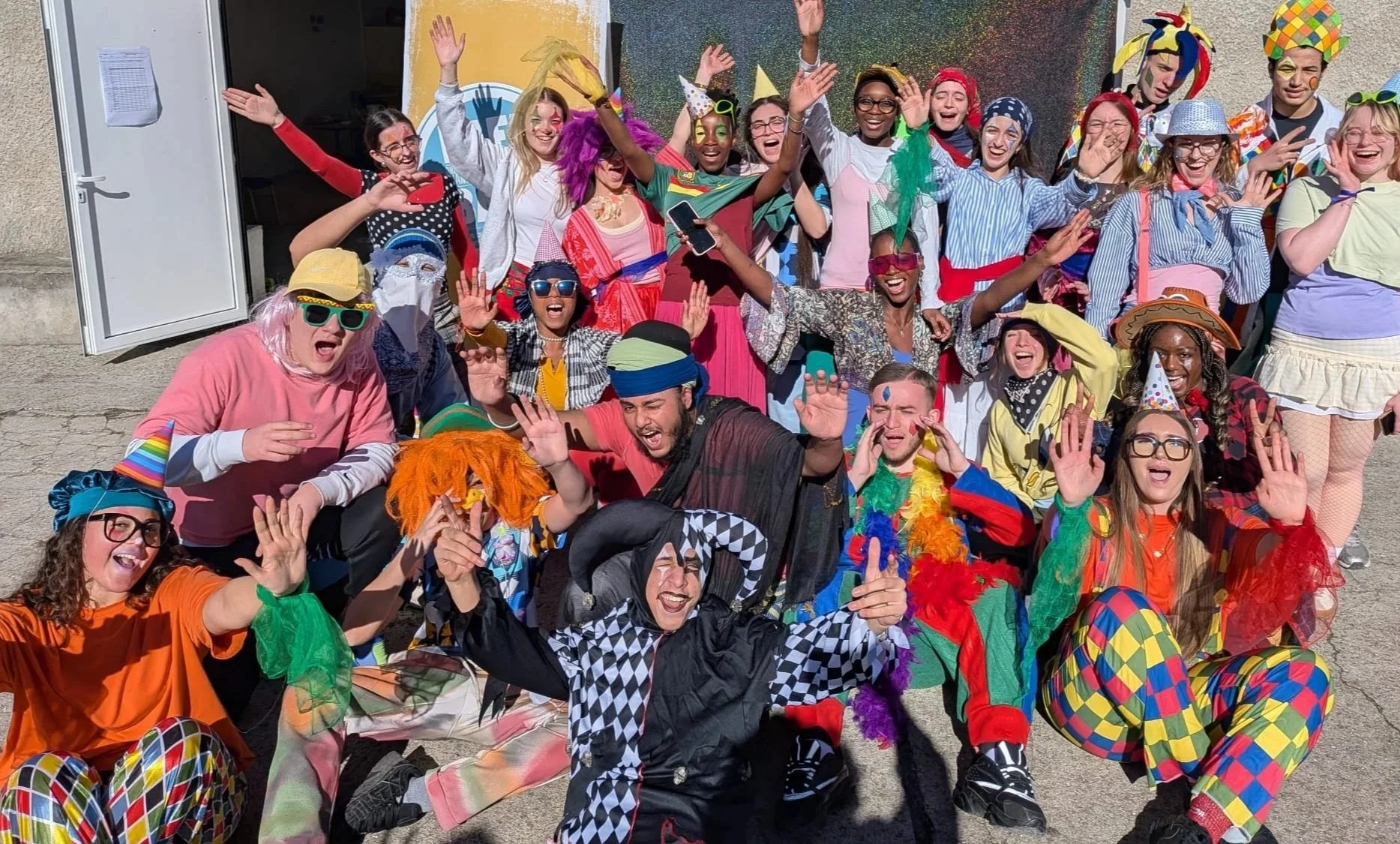 Groupe de personnes déguisées en clown et en personnages de carnaval posant pour une photo avec des sourires et des gestes joyeux.