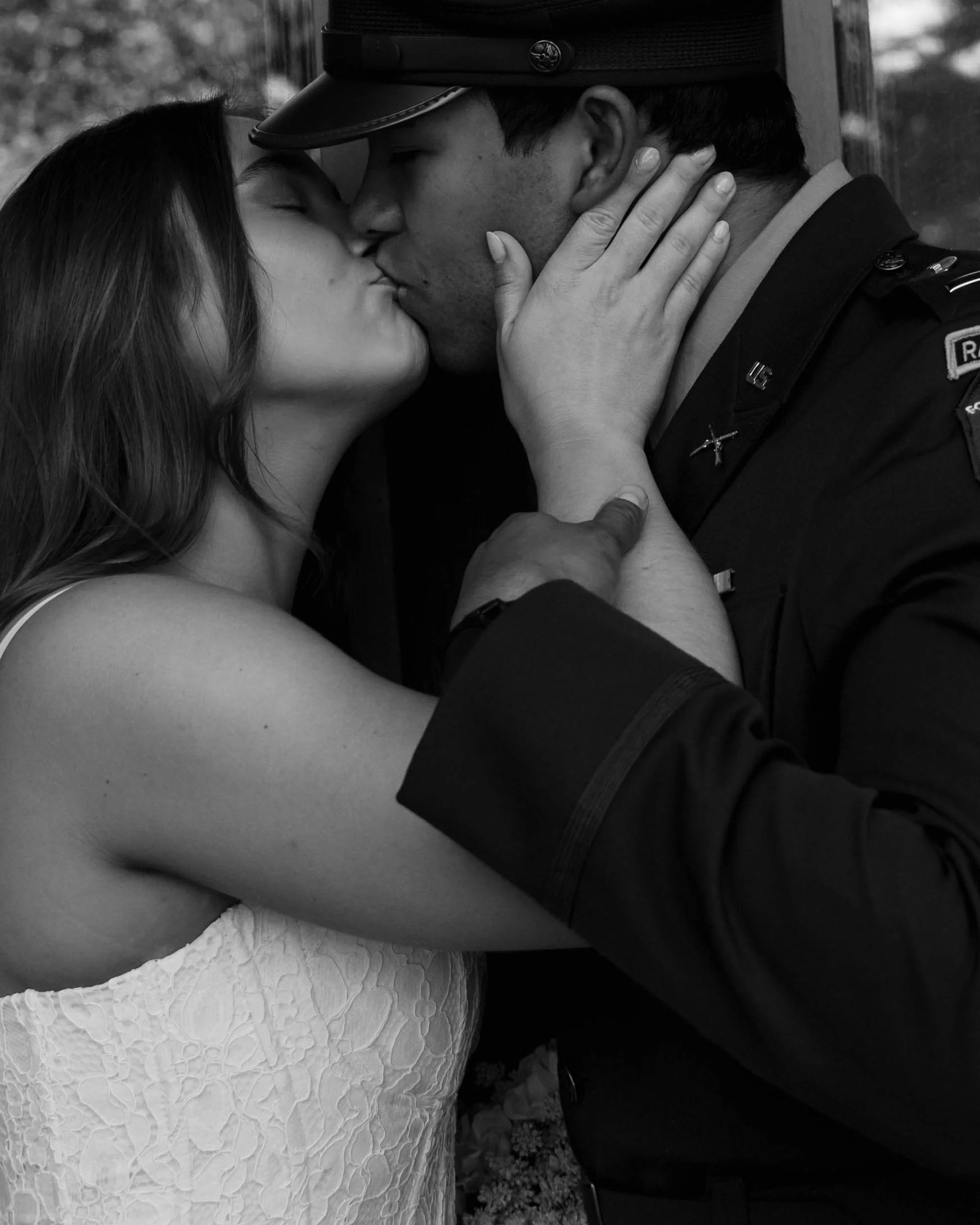 A black and white photograph of a couple sharing a kiss, with the woman holding the man's face and the man in a military uniform.