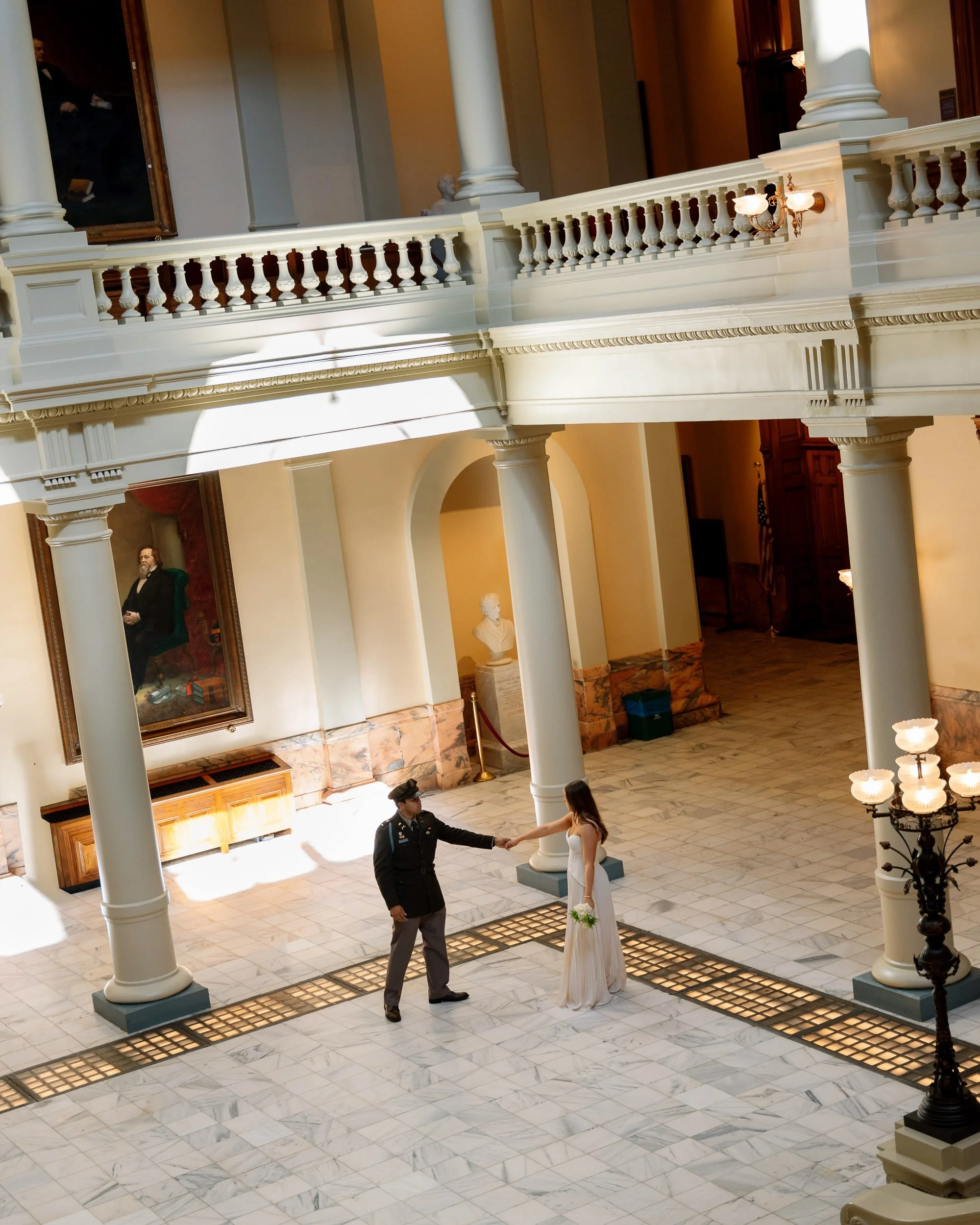 A bride in a white wedding dress holding a bouquet shaking hands with a police officer inside a grand, elegant building with marble floors, tall columns, and classical architecture.