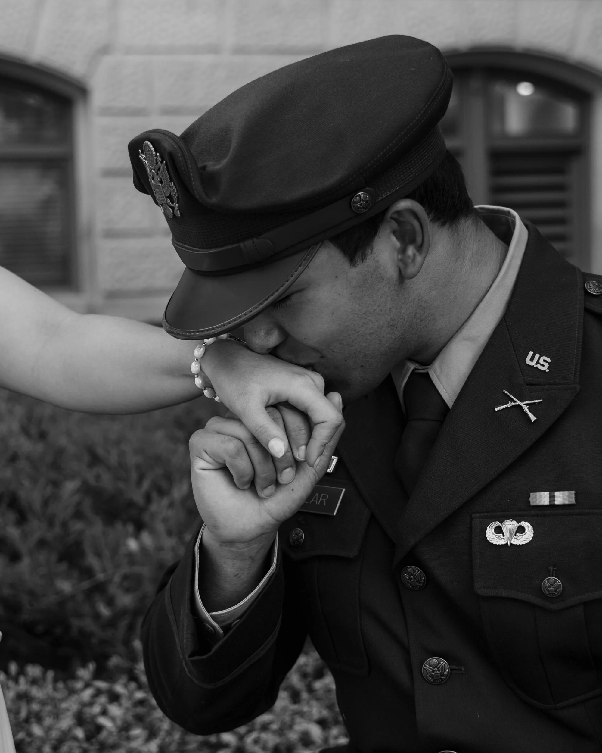 A soldier wearing a U.S. Army uniform and hat is kissing a woman's hand.