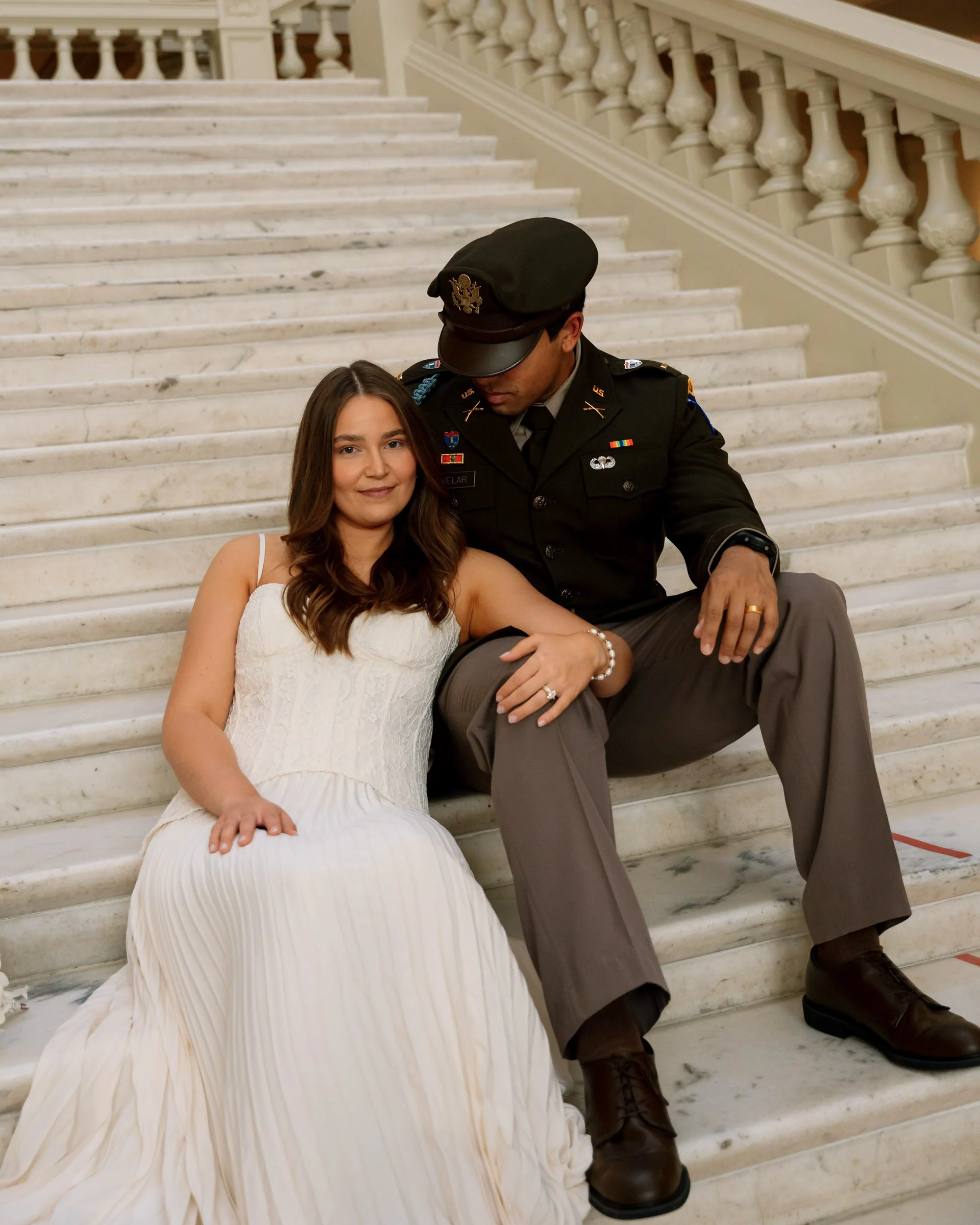 A woman in a white dress and a man in a military uniform sitting on marble stairs.