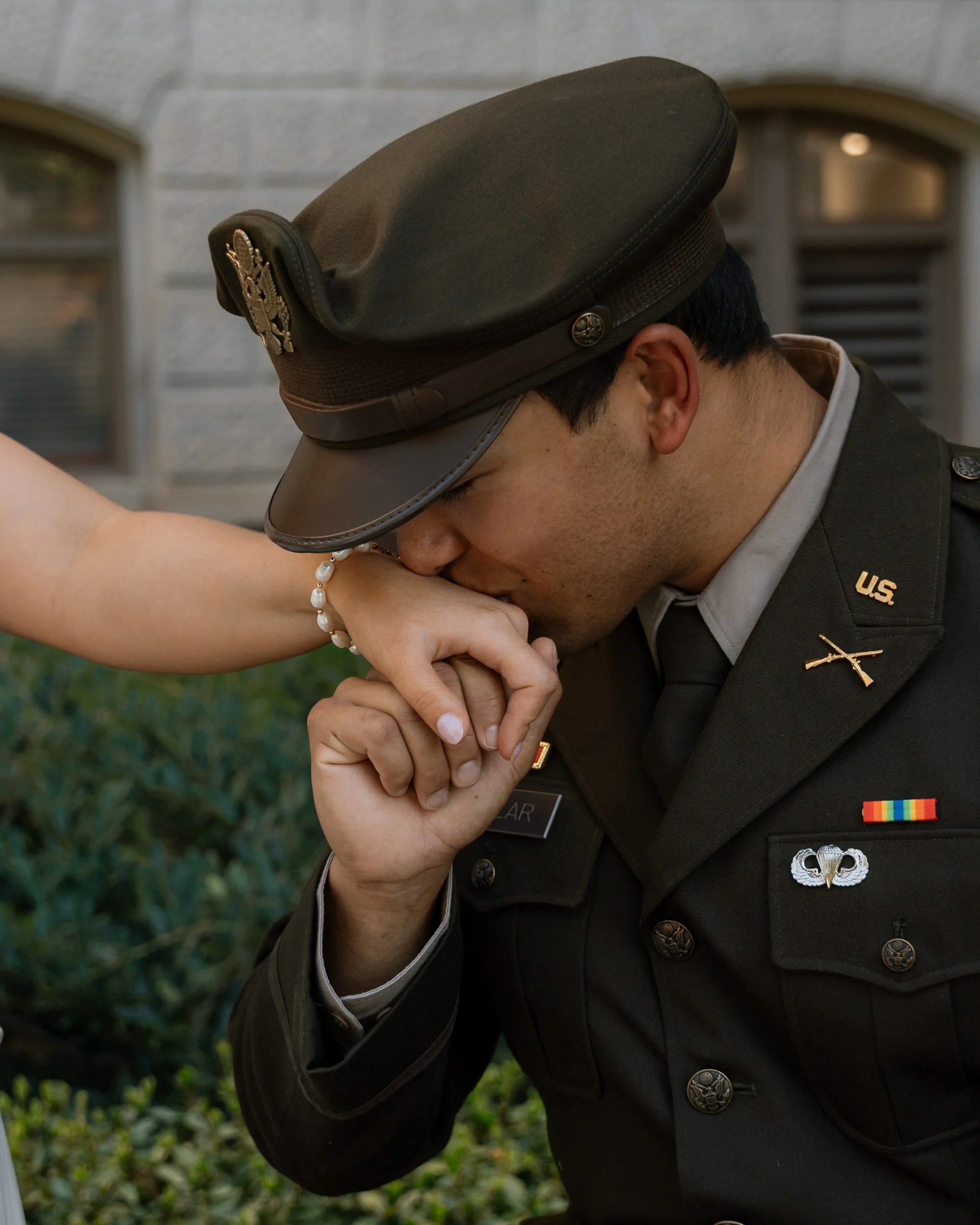 A soldier in a U.S. Army uniform kissing a woman's hand outdoors.