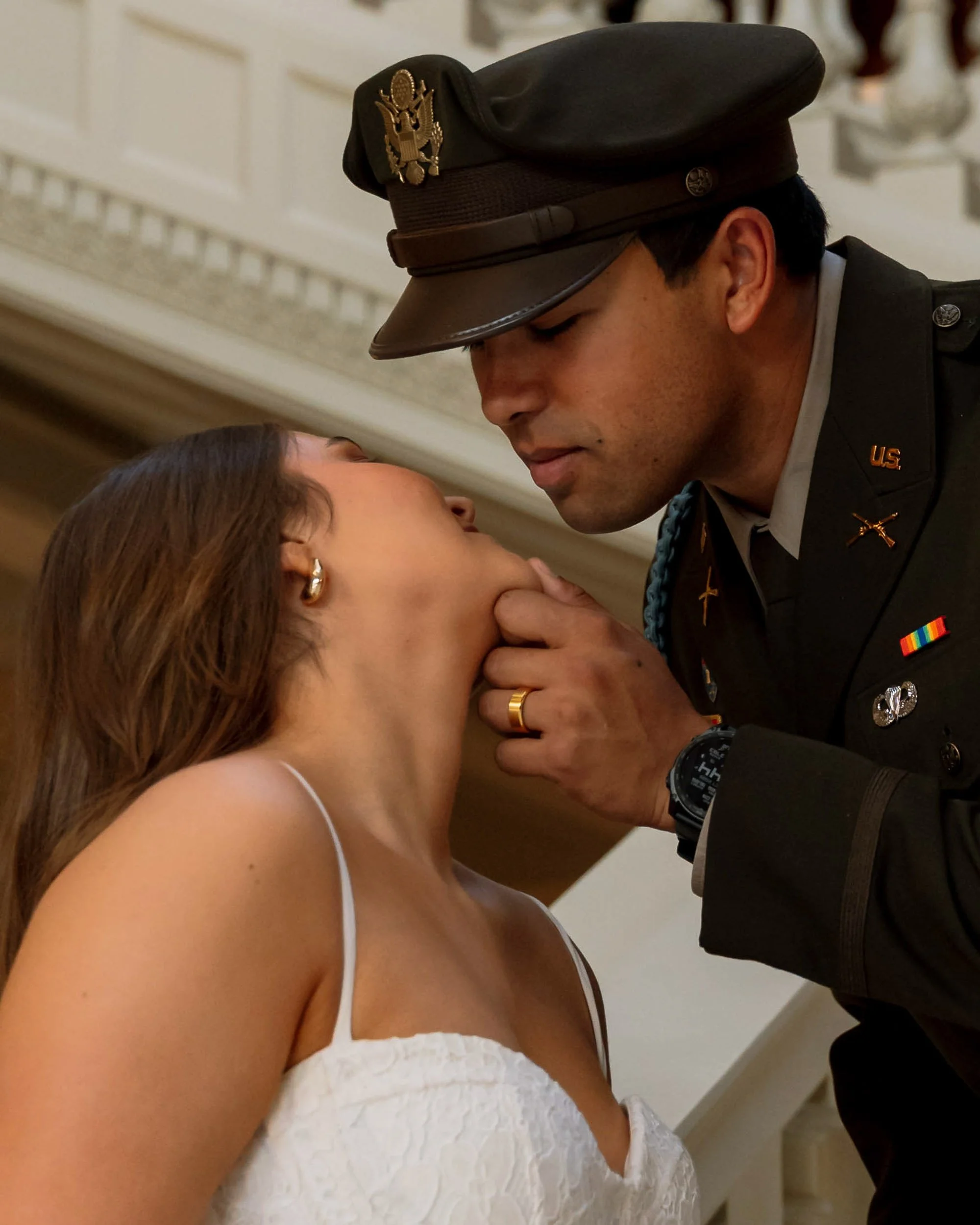 A man in a U.S. Army uniform and a woman in a white dress are in an intimate moment, with the man holding the woman's chin and leaning in close to her face.