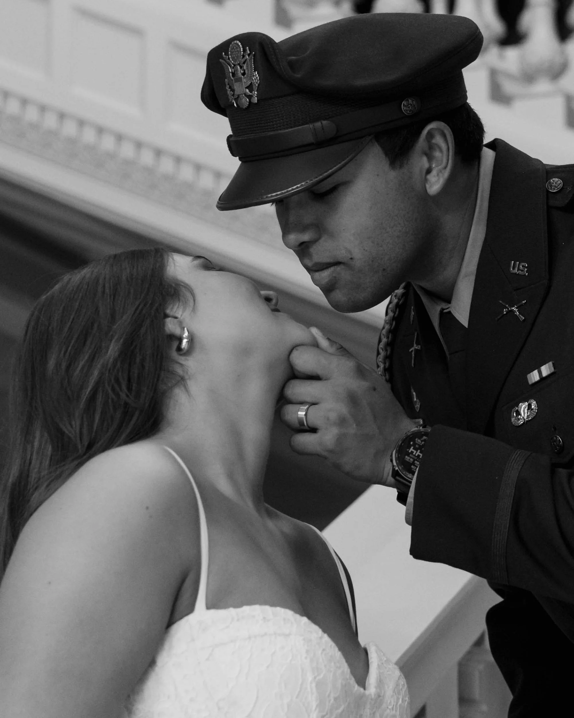 A soldier in uniform leaning close to a woman, gently touching her chin, in a tender moment. The woman has shoulder-length hair and earrings, wearing a sleeveless top.