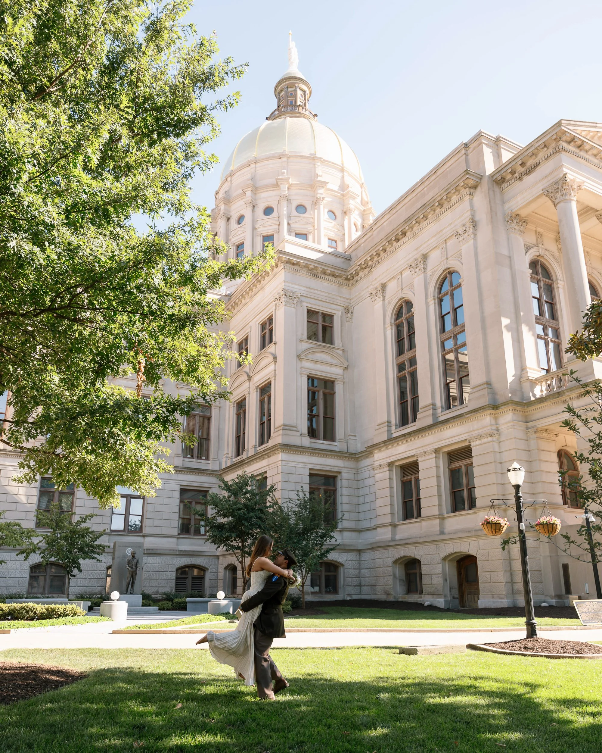 A couple dancing outside a historic white stone building with a large dome and tall windows, surrounded by trees and street lamps.