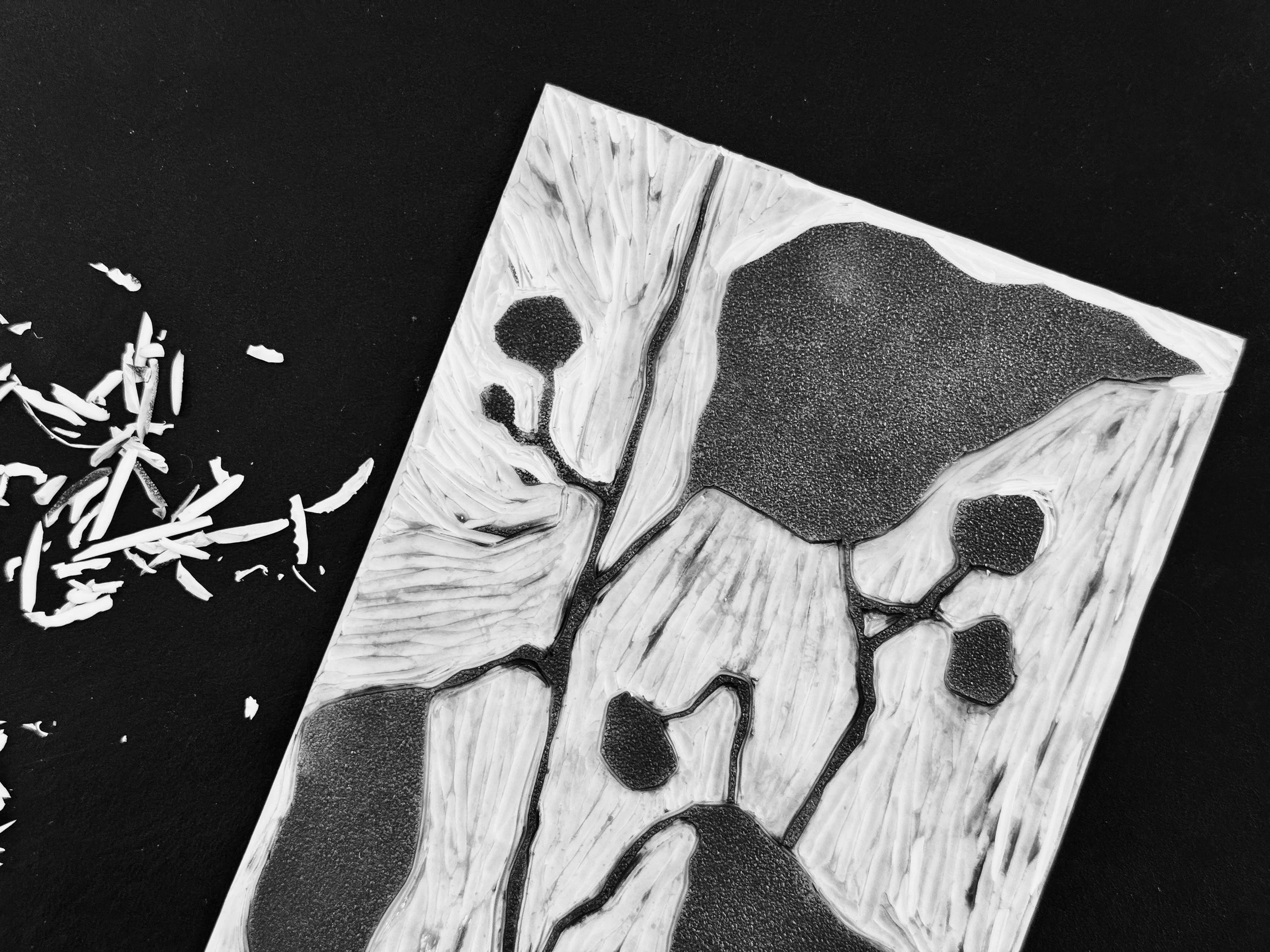 A black and white abstract art piece with geometric shapes, textured patterns, and scattered shredded paper on a flat surface.