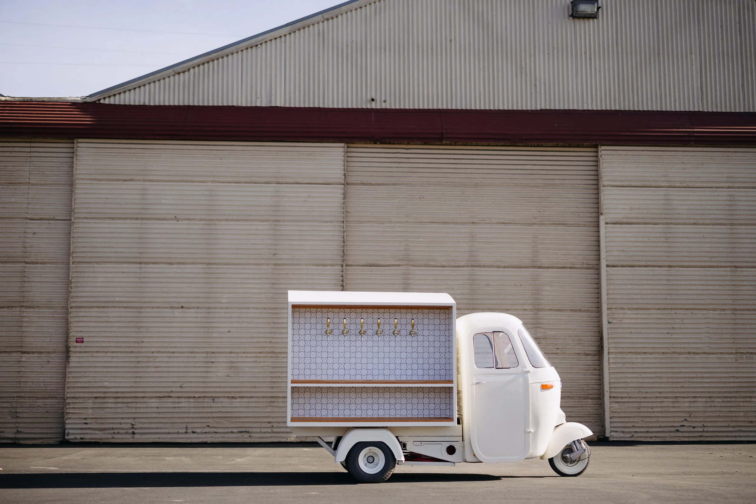 Vintage Piaggio Ape converted into a six-tap mobile bar with patterned tile and hardwood shelving