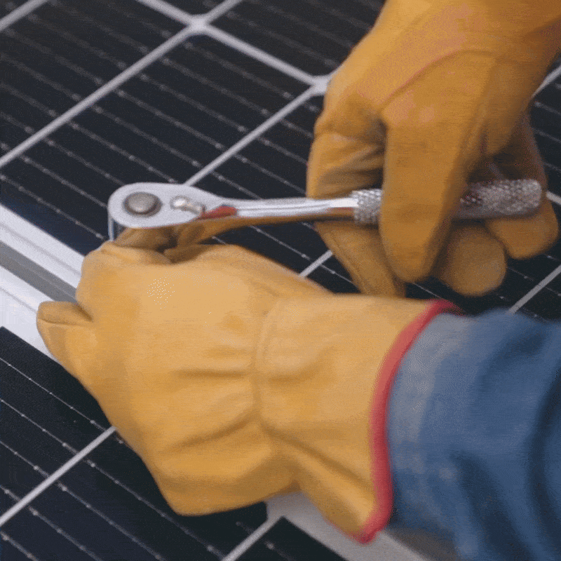 Qualcuno stringe un attrezzo con una mano guantata di giallo, mentre lavora su un pannello solare.