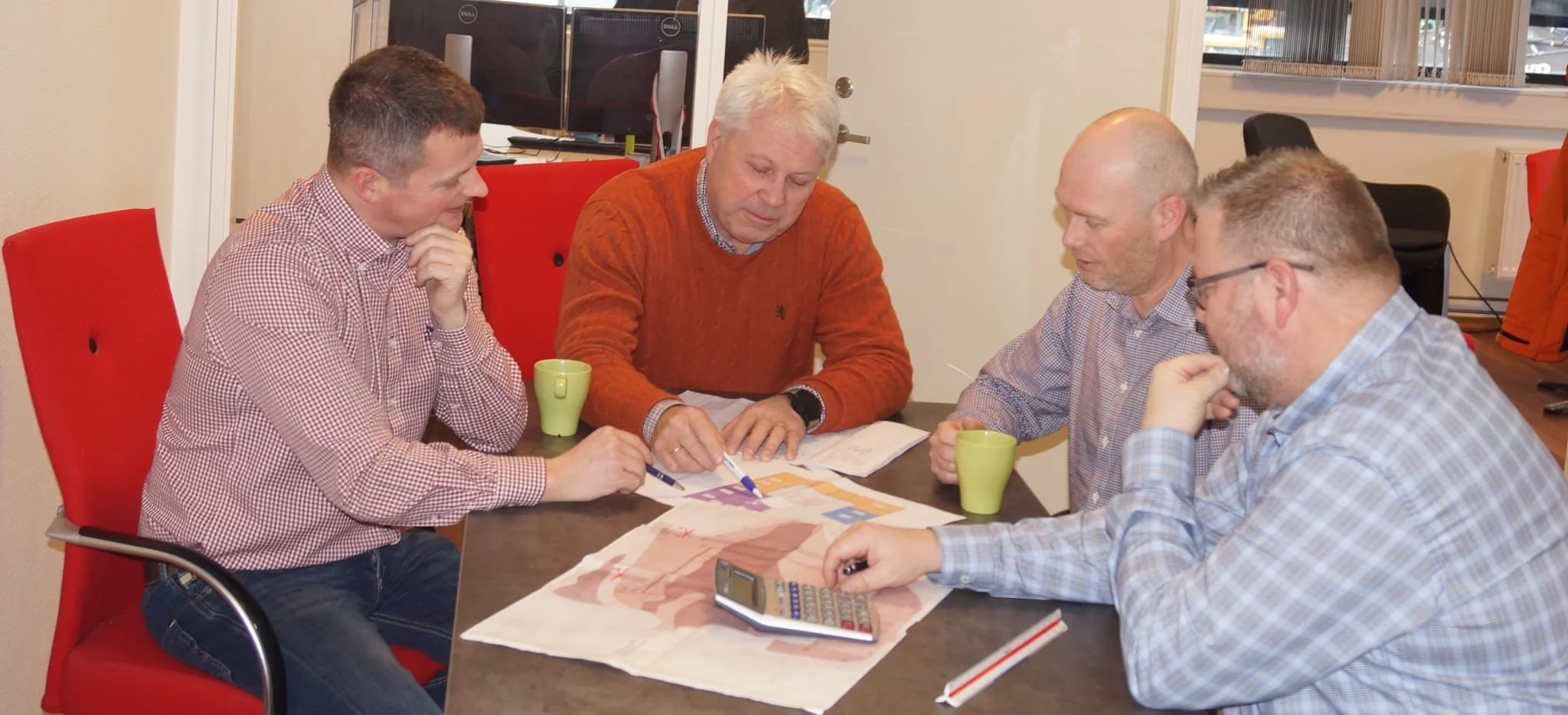 Fem menn sitter rundt et bord og diskuterer et kart eller diagram.