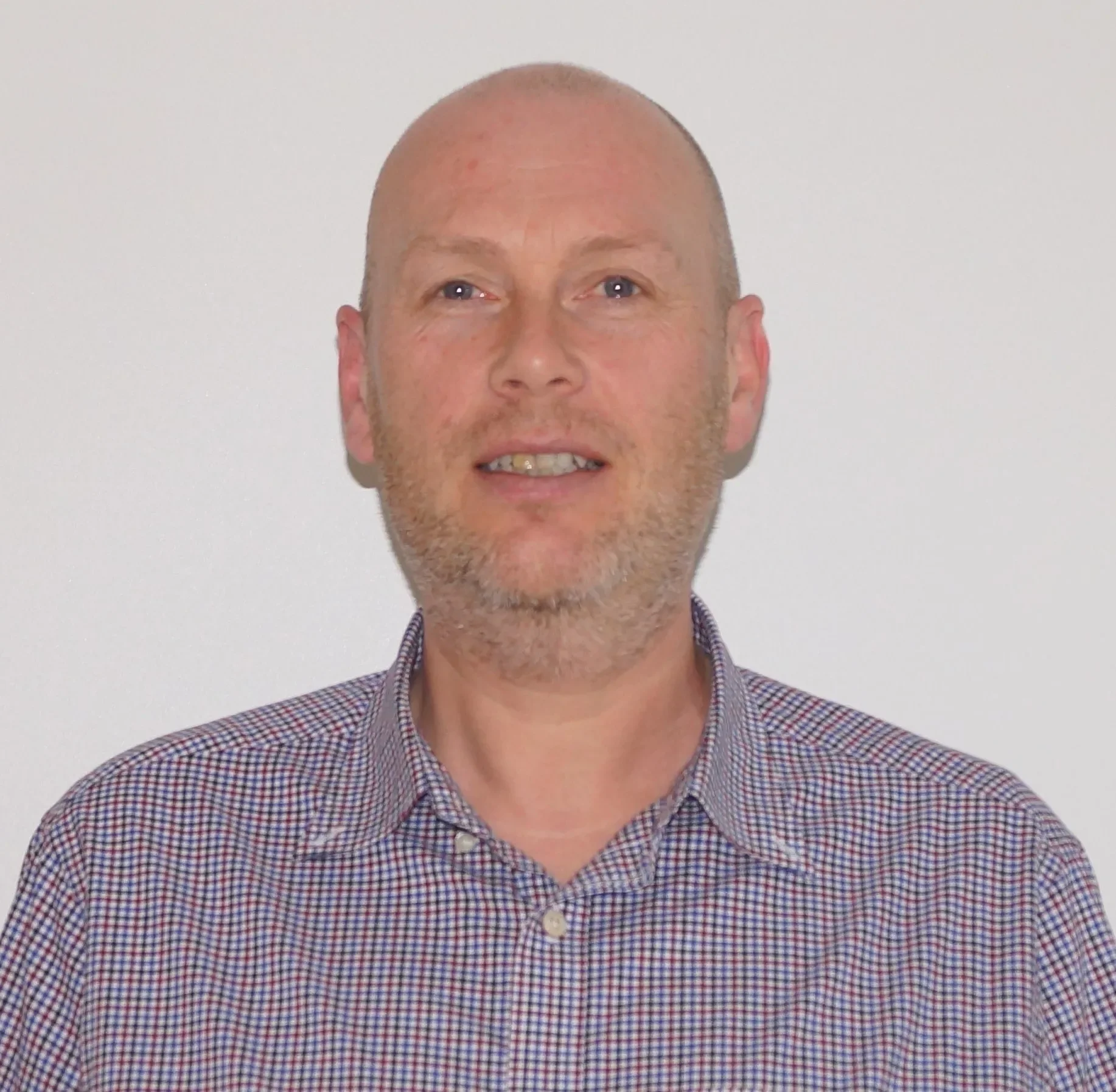 Portrett av en mann med skjegg, blonde hår og blå øyne, iført en sjakett med små rutemønster, mot en lys bakgrunn.