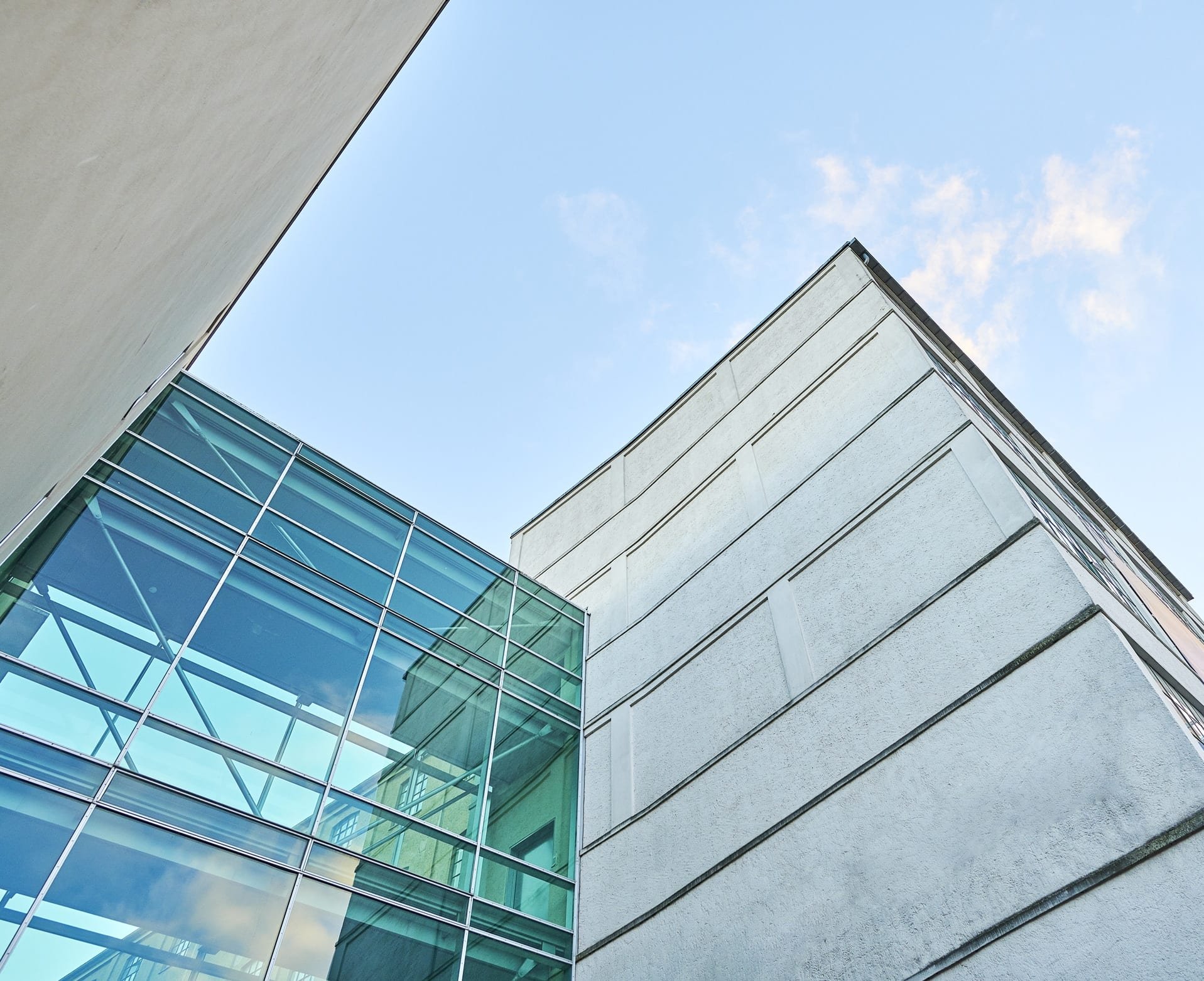 Fasade av moderne bygning med glassvinduer og hvitelagt murverk mot en blå himmel.