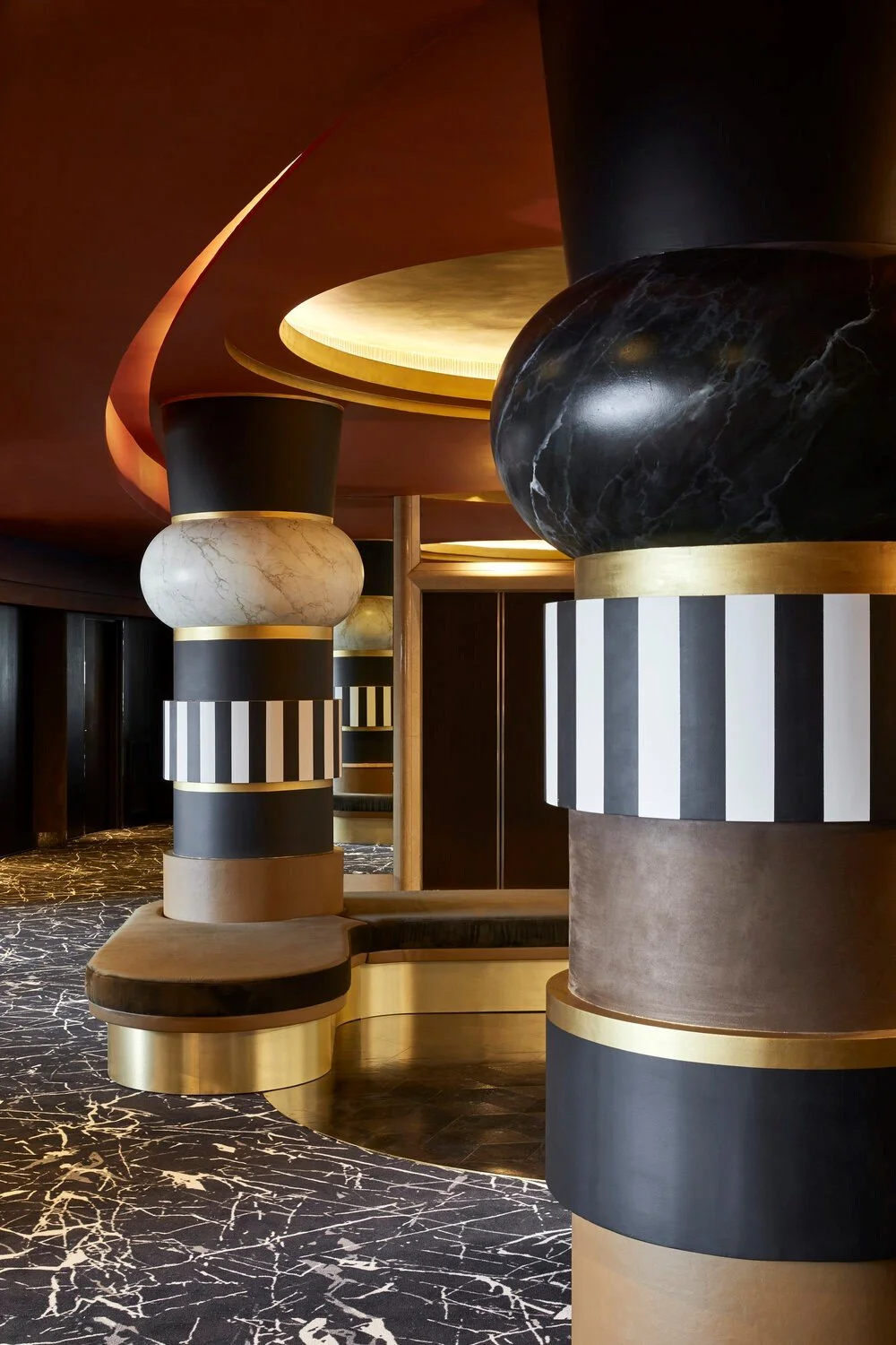 Modern interior design featuring black and white striped columns with gold accents, a marble-patterned floor, and curved ceiling elements.