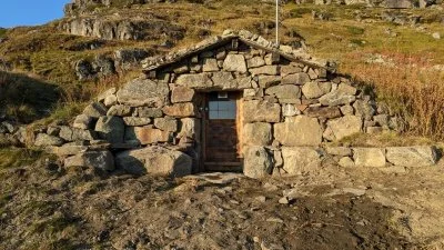 En steinbygning med en liten dør, omgitt av hverdaglig terreng og fjell.
