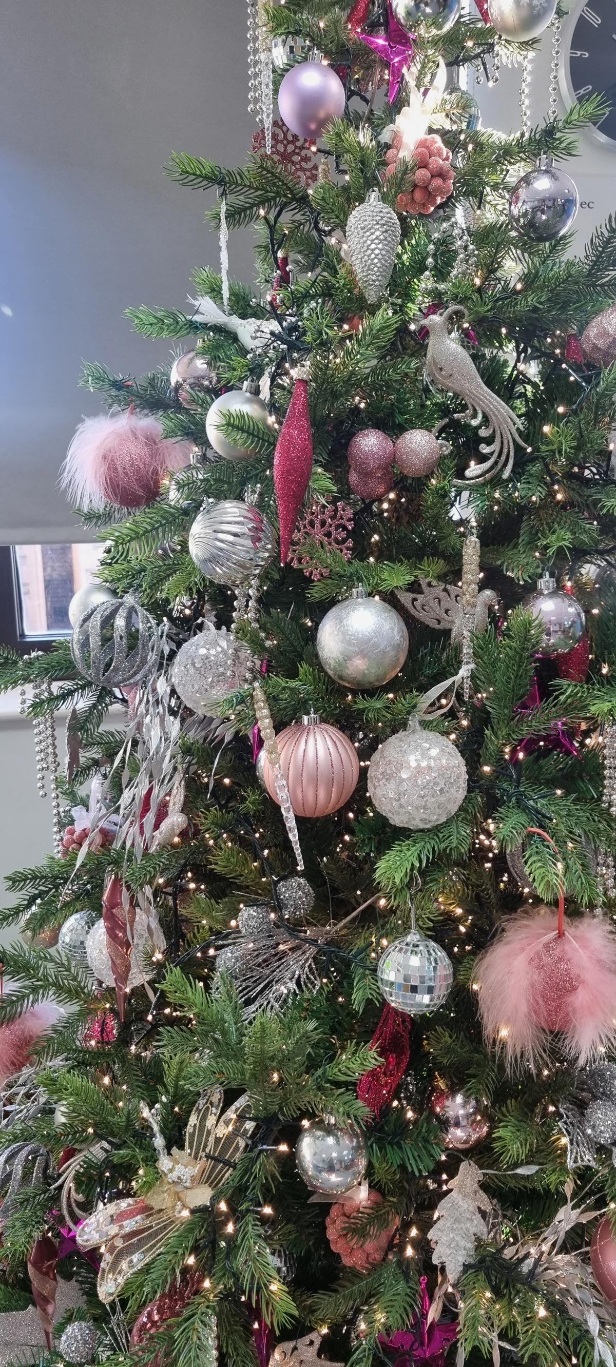 Decorated Christmas tree with pink, silver, white, and glittery ornaments, baubles, and lights.