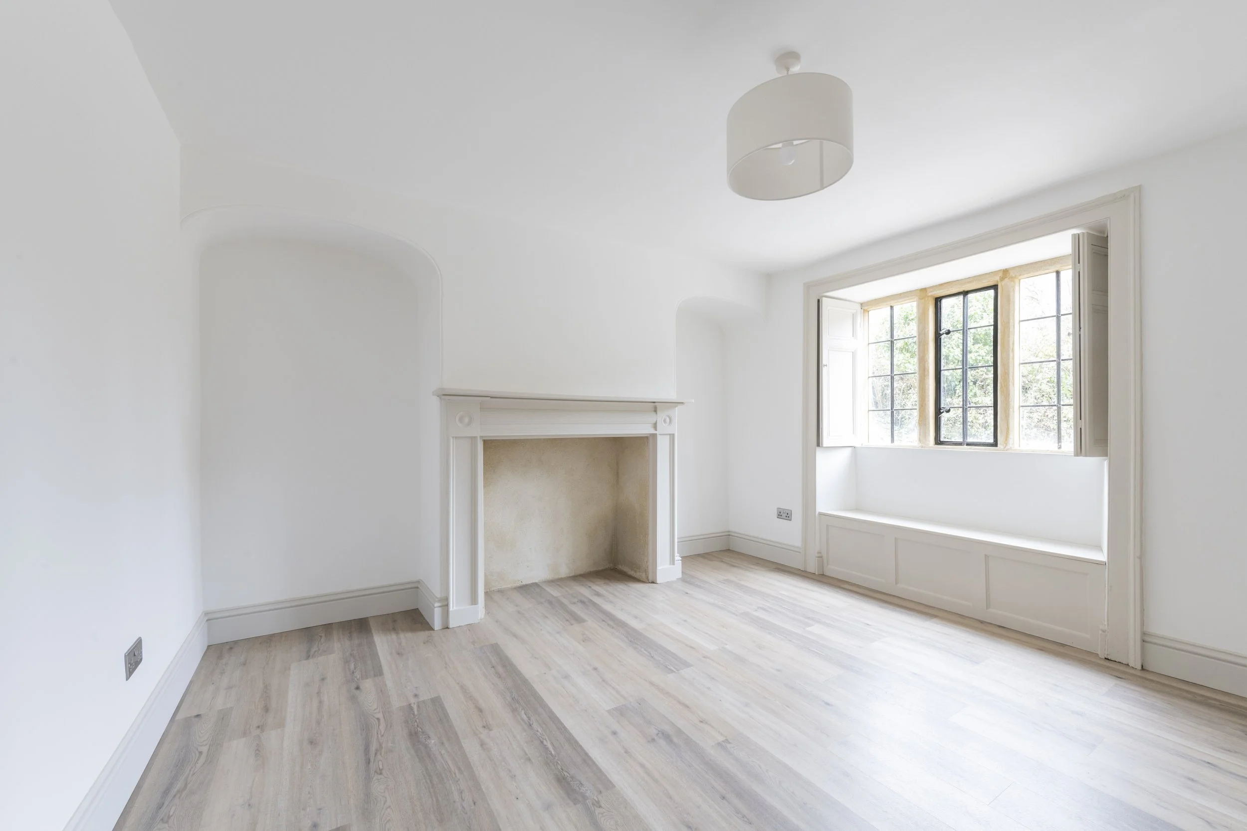 Empty bright white room with a large window, a fireplace, and wooden flooring.