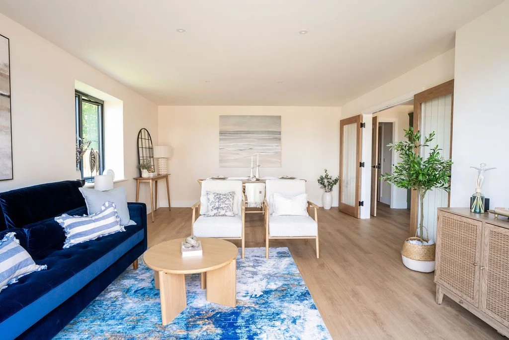 Staged show home living area. Blue sofa, blue rug, 2 armchairs & dining table