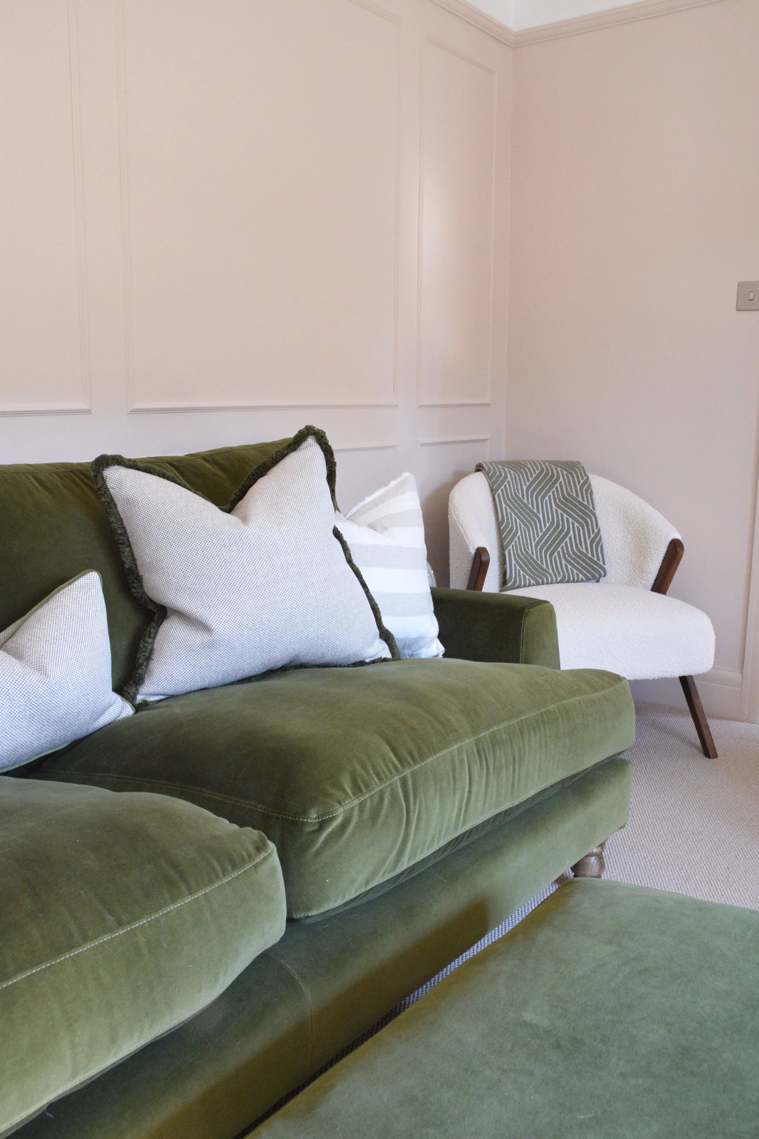 Living room with a green velvet sofa with white and striped pillows, and a white armchair with a gray patterned throw.