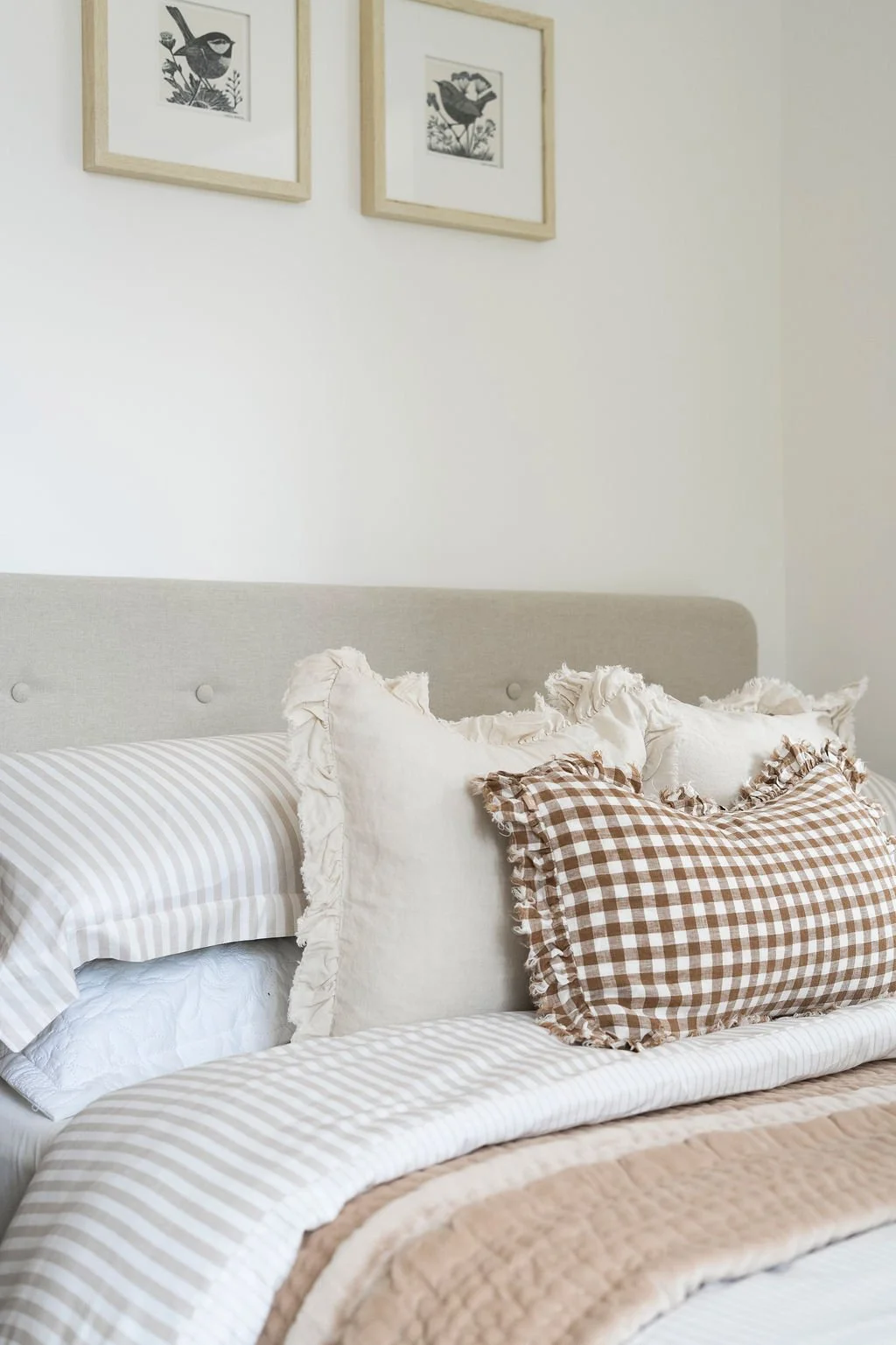 Double bed dressed with a neutral stiped duvet, velvet throw & gingham cushion