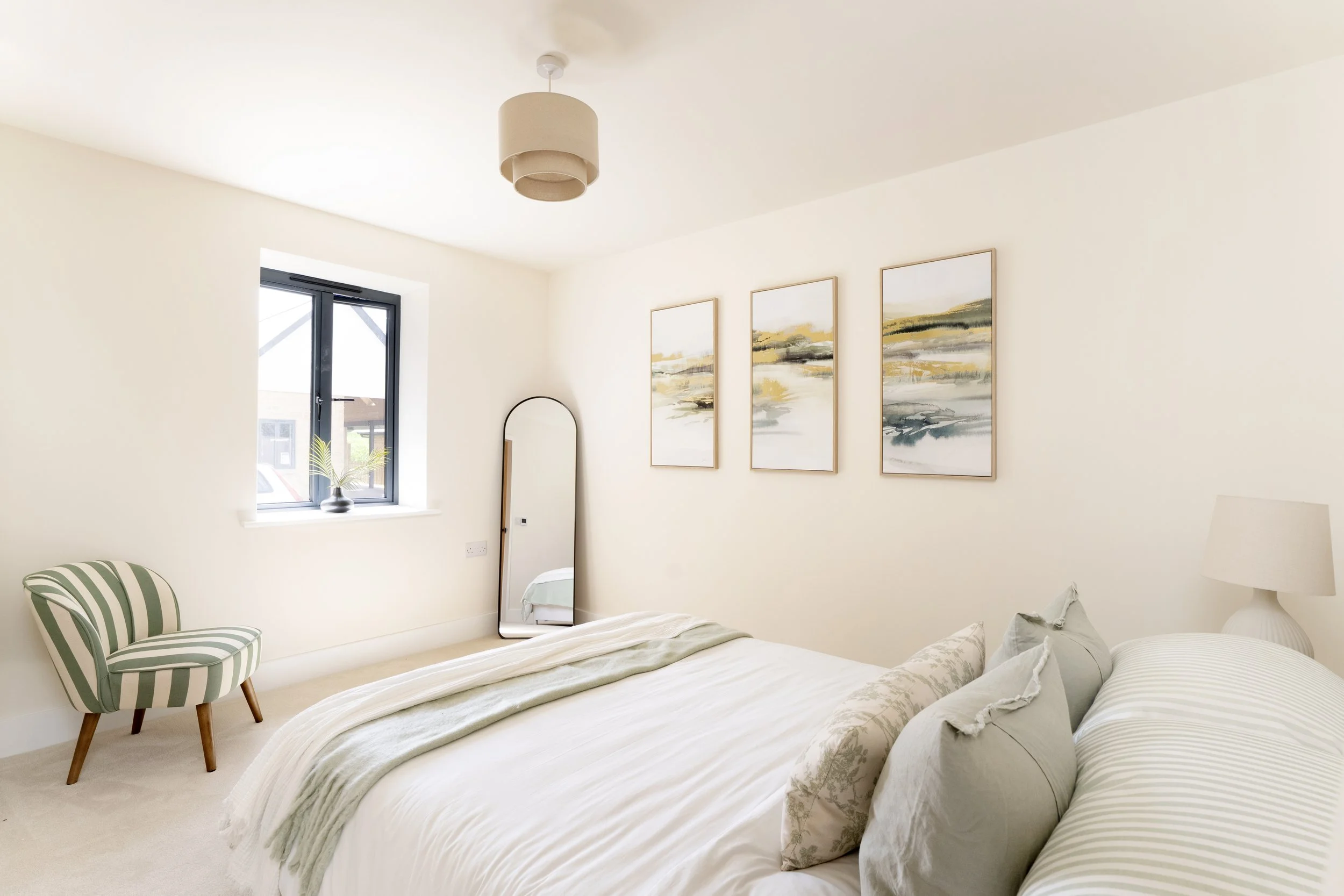 Professionally staged bedroom in a Somerset property with soft green bedding, striped accent chair and neutral furnishings. Floor mirror & triple canvas pictures on wall.
