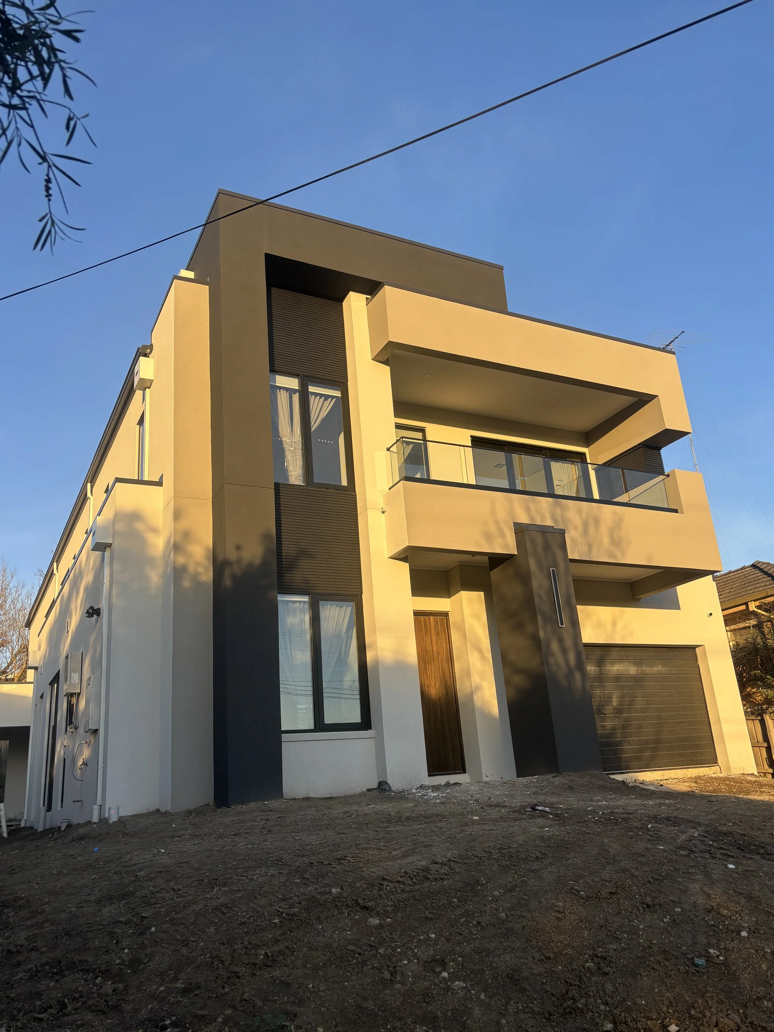 Modern, multi-story residential building with balconies, large windows, and a garage, taken during sunset.