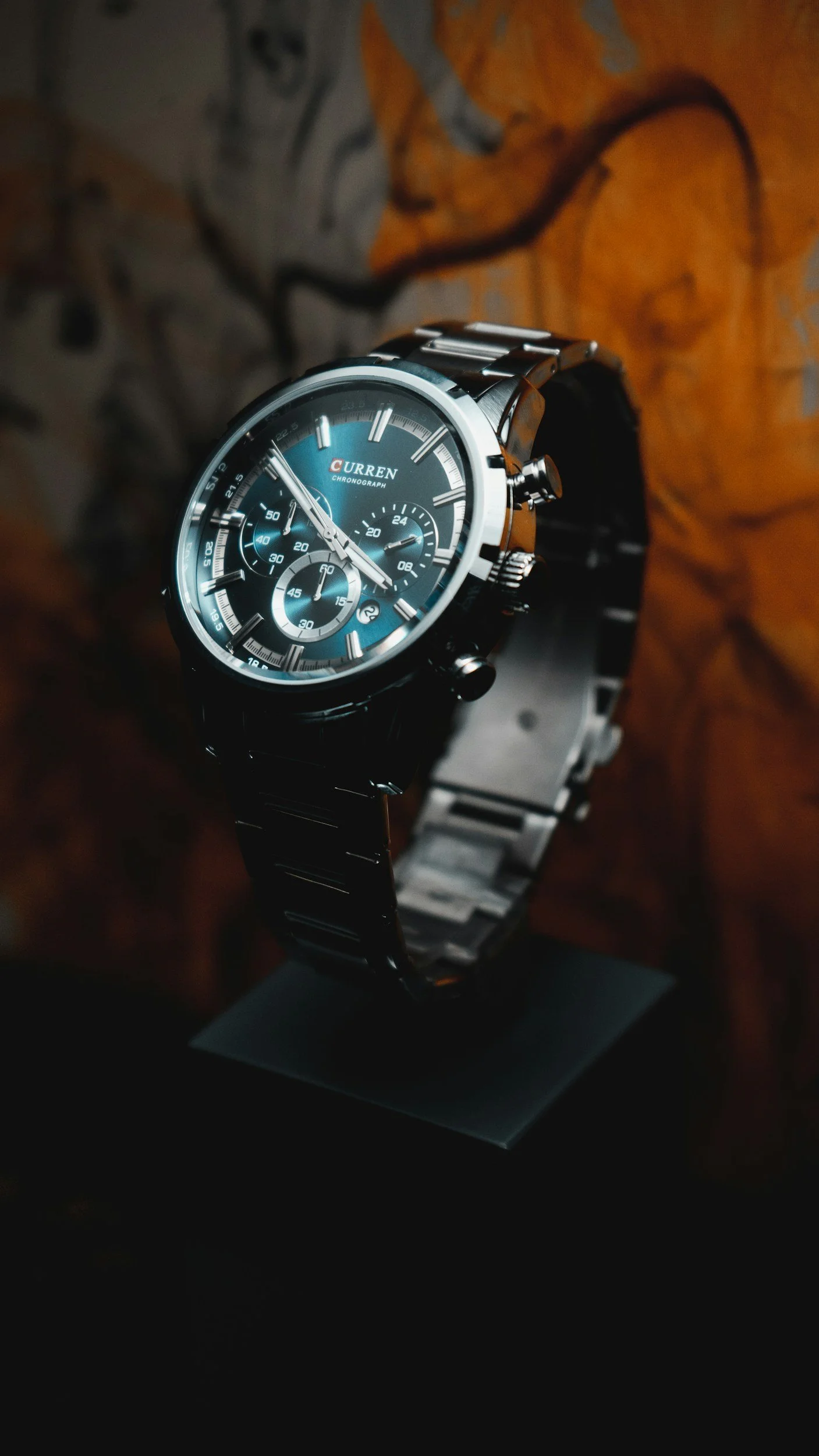Eine schwarze Armbanduhr mit einem blauen Zifferblatt und mehreren kleinen Zifferblättern, auf einem schwarzen T-Stand mit Holzmaserung im Hintergrund.