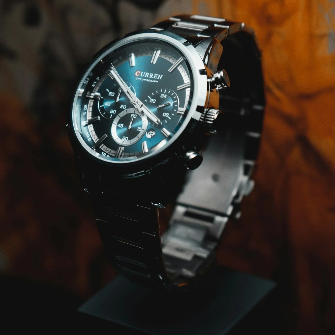 Ein schwarzer Armbanduhr mit blauer Zifferblatt, Chronographenfunktionen und Metallarmband, auf Holzuntergrund.