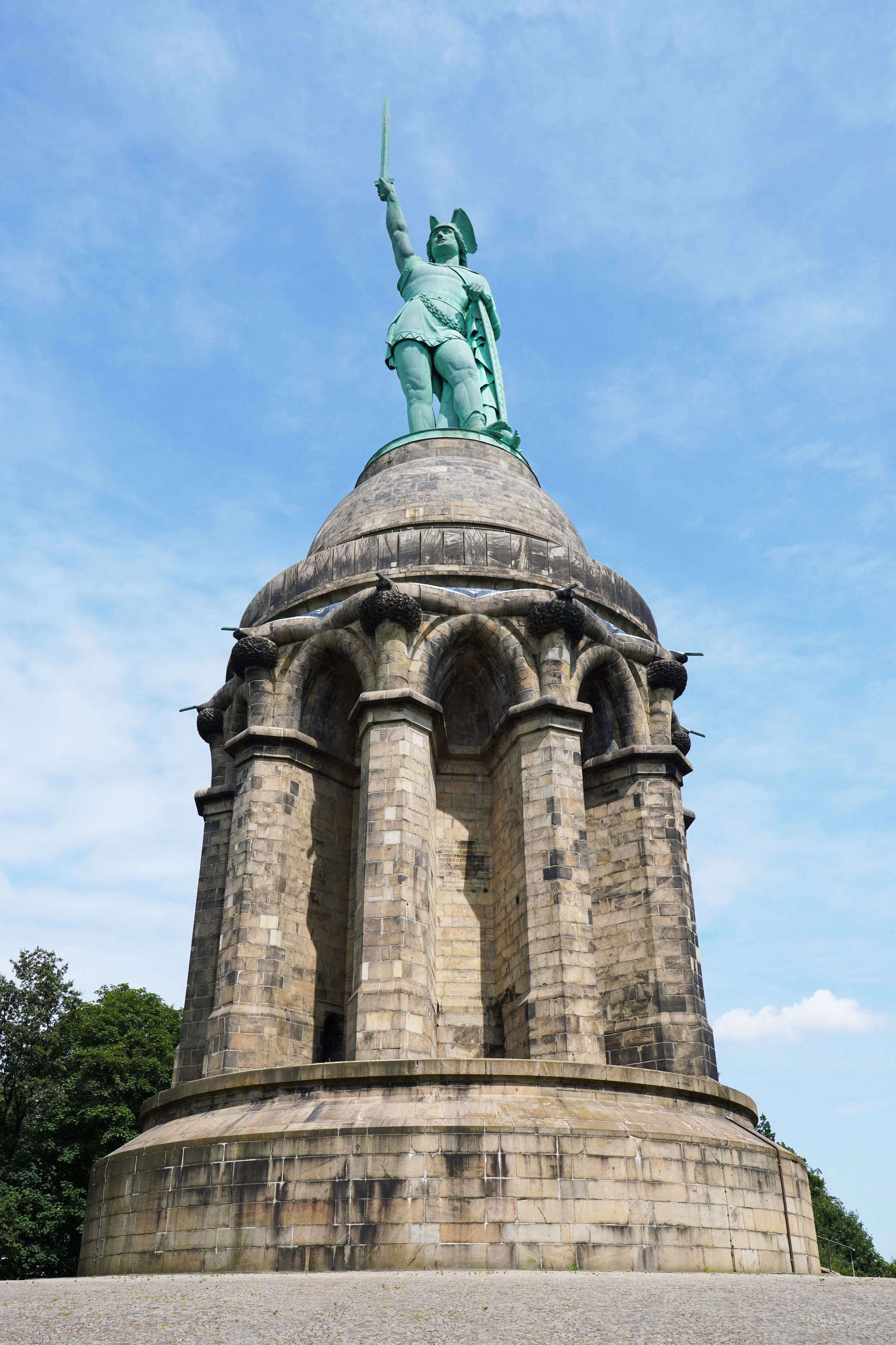 Denkmal mit Statue eines römischen Soldaten auf einer steinernen Säule unter blauem Himmel.