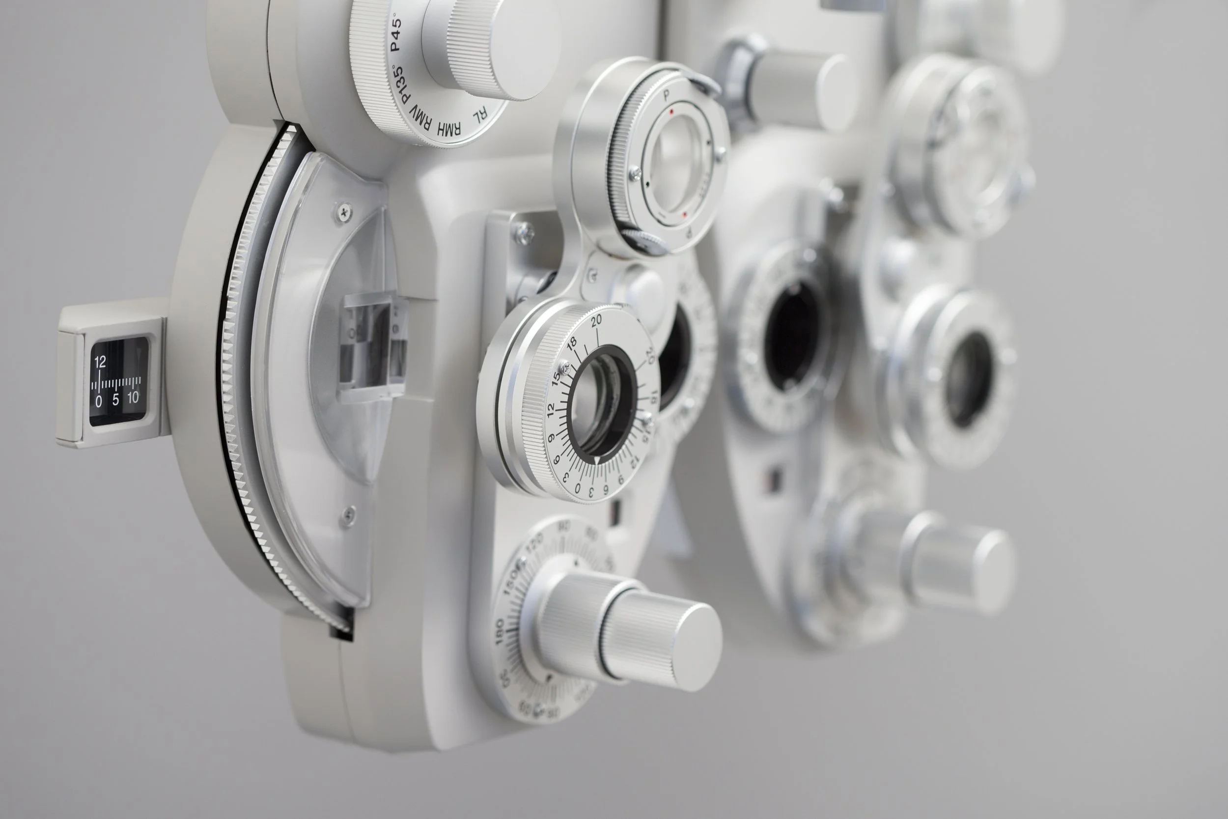 Nahaufnahme eines weißen ophthalmologischen Untersuchungsgeräts mit mehreren Einstellknöpfen und Skalen.