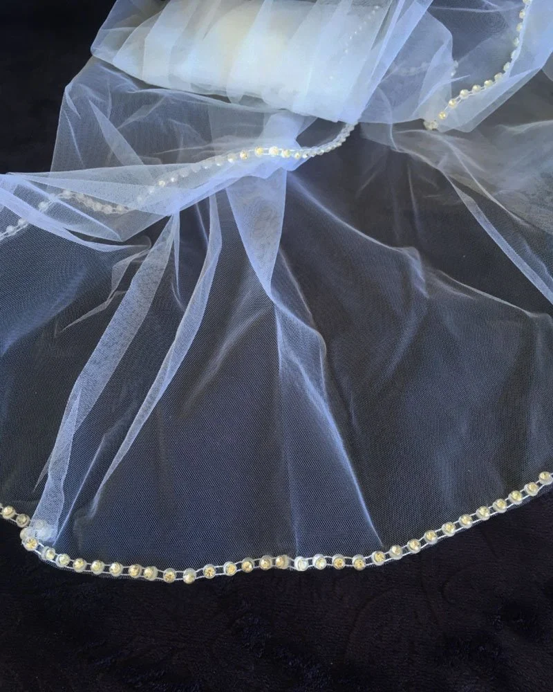 Close-up of sequin and beaded diamanté trim on bridal veil edge, delicate sparkle on soft tulle fabric.