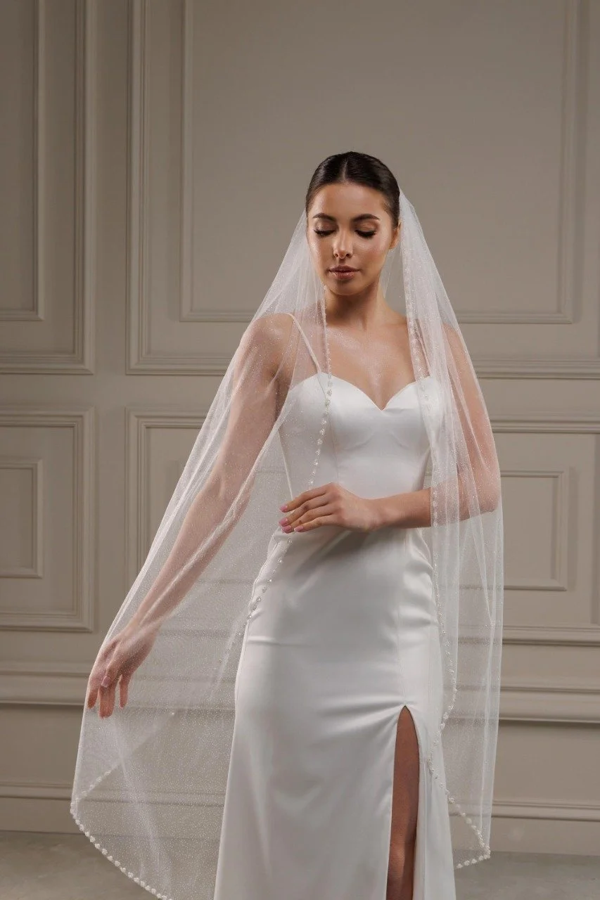 Bride wearing knee length pearl beaded edge glitter wedding veil in off white color