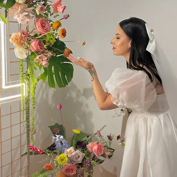 A bride in a white dress and a cute bow veil is placing flowers in a floral arrangement.