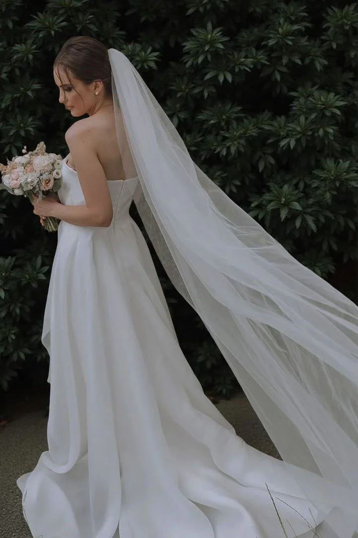 Side view of bride wearing a simple clean plain single layer wedding veil in cathedral length.
