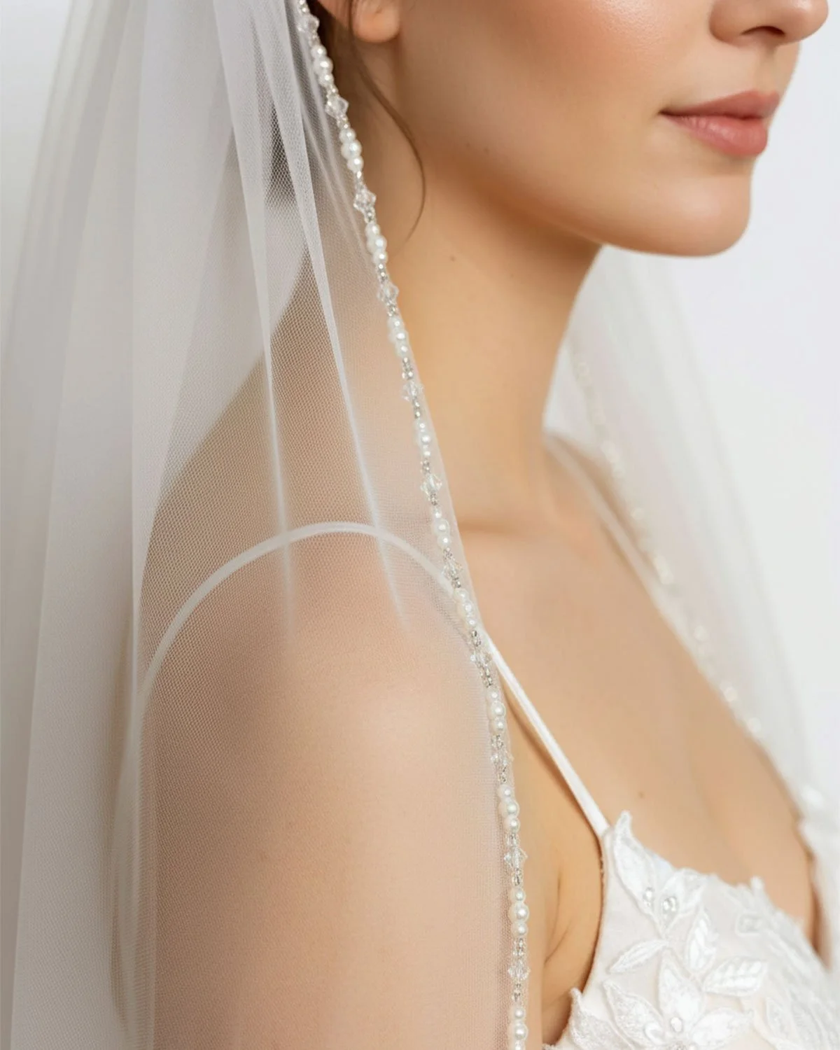 Close up detail of a beaded pearl trim single tier custom lengths wedding veil in off white, ivory and champagne tulle.