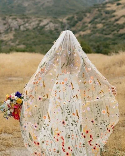 Bride wearing colorful wildflower embroidered veil, a floral appliqué design trending in 2026 wedding veil styles.