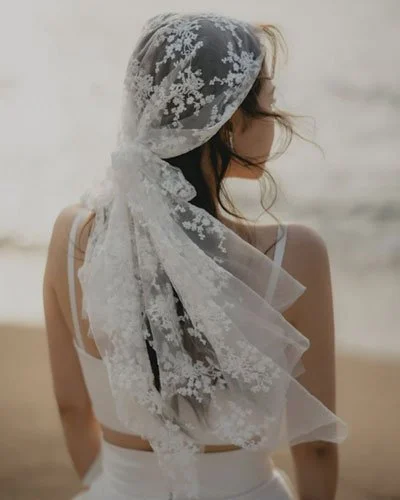 Back view of bride wearing practical head scarf veil on beach, venue-aware style reflecting 2026 wedding veil trends.