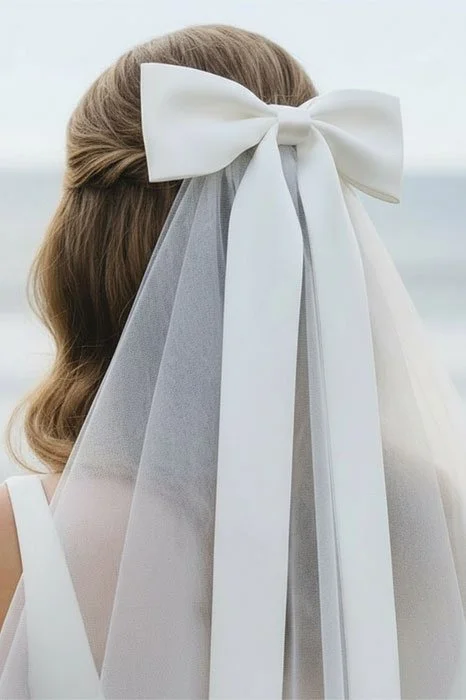 Close up back view of bride wearing a short shoulder length satin ribbon bow wedding veil in off white tulle color.